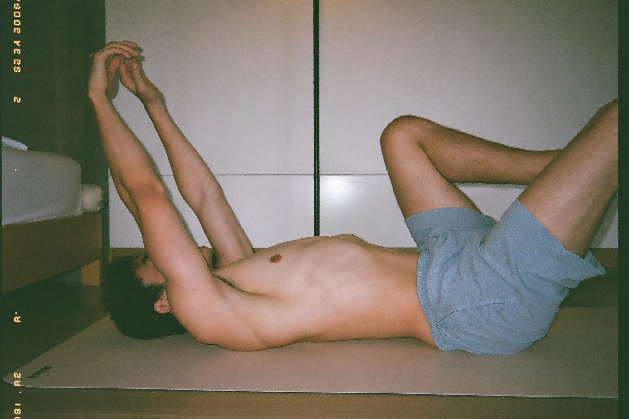 Man performing a dead bug exercise on a mat at home, arms raised and lower back pressed flat to the floor