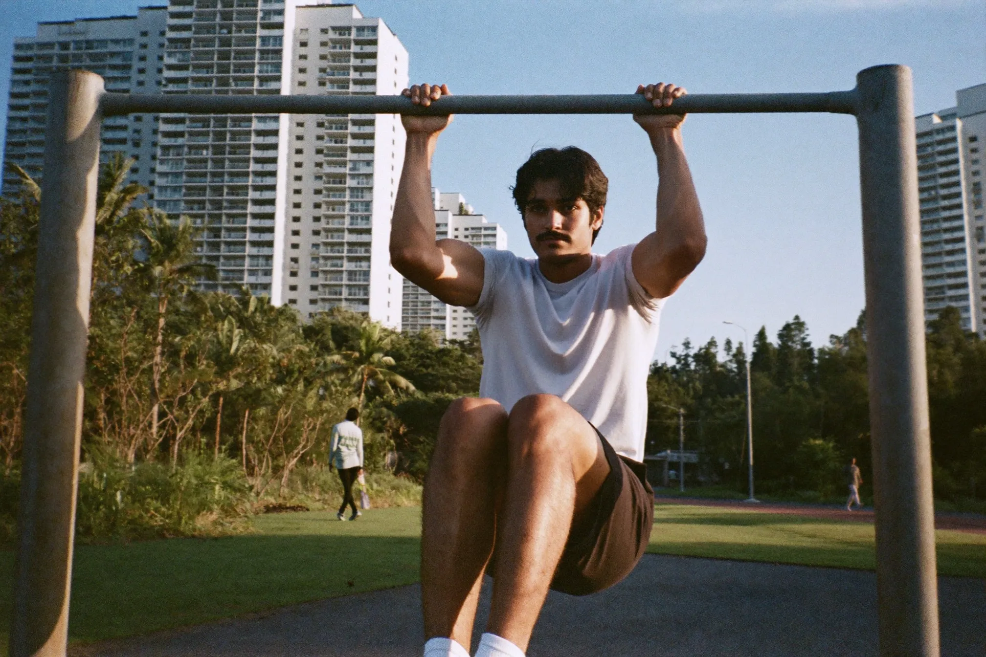 Man doing hanging knee raises on a pull-up bar at an outdoor fitness corner between apartment blocks