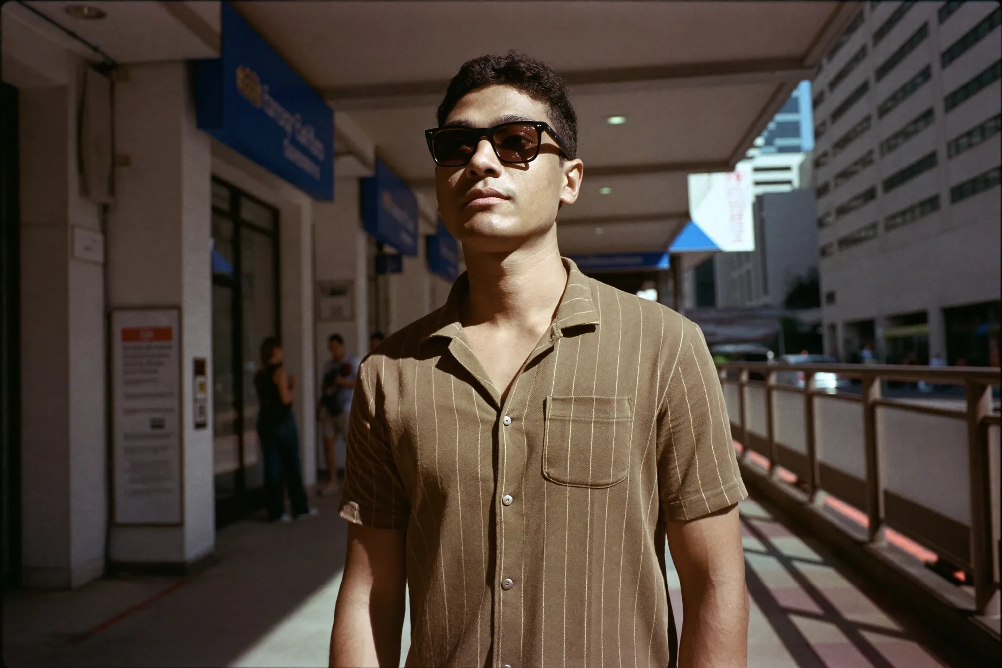 Man in dark sunglasses waiting at a covered walkway in Singapore's CBD during bright midday glare
