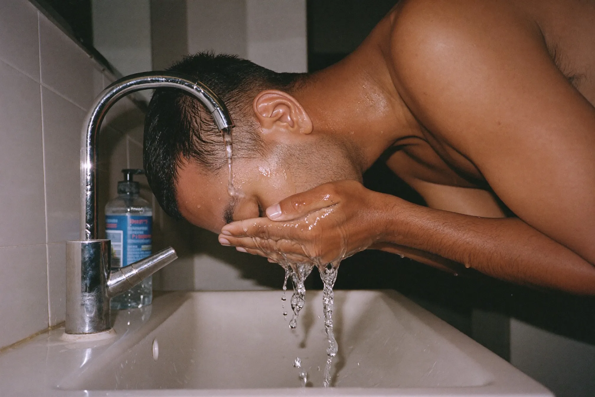 Man rinsing his face with water over a bathroom sink after cleansing