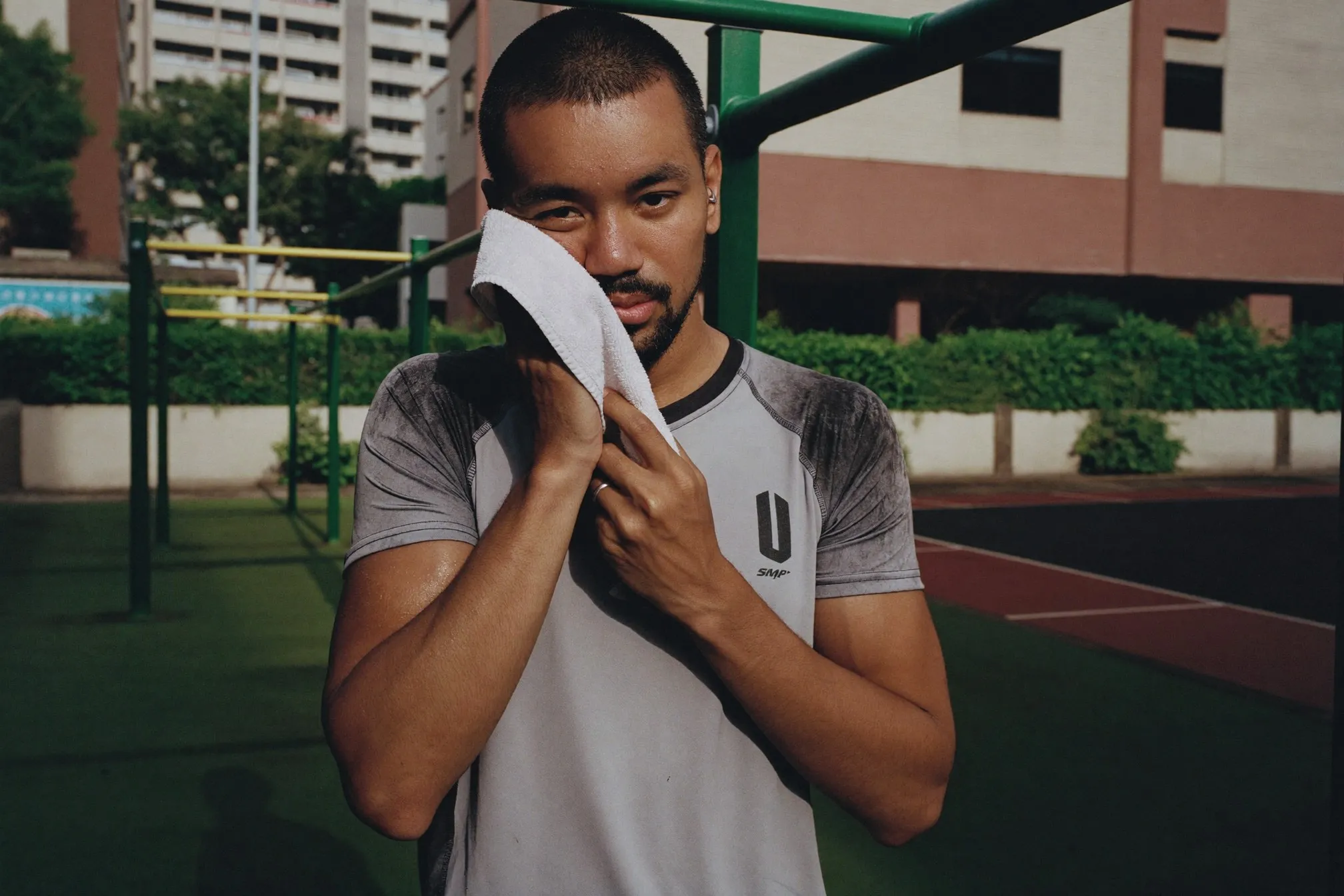 Man wiping sweat from his face with a small towel after exercising at an outdoor fitness corner