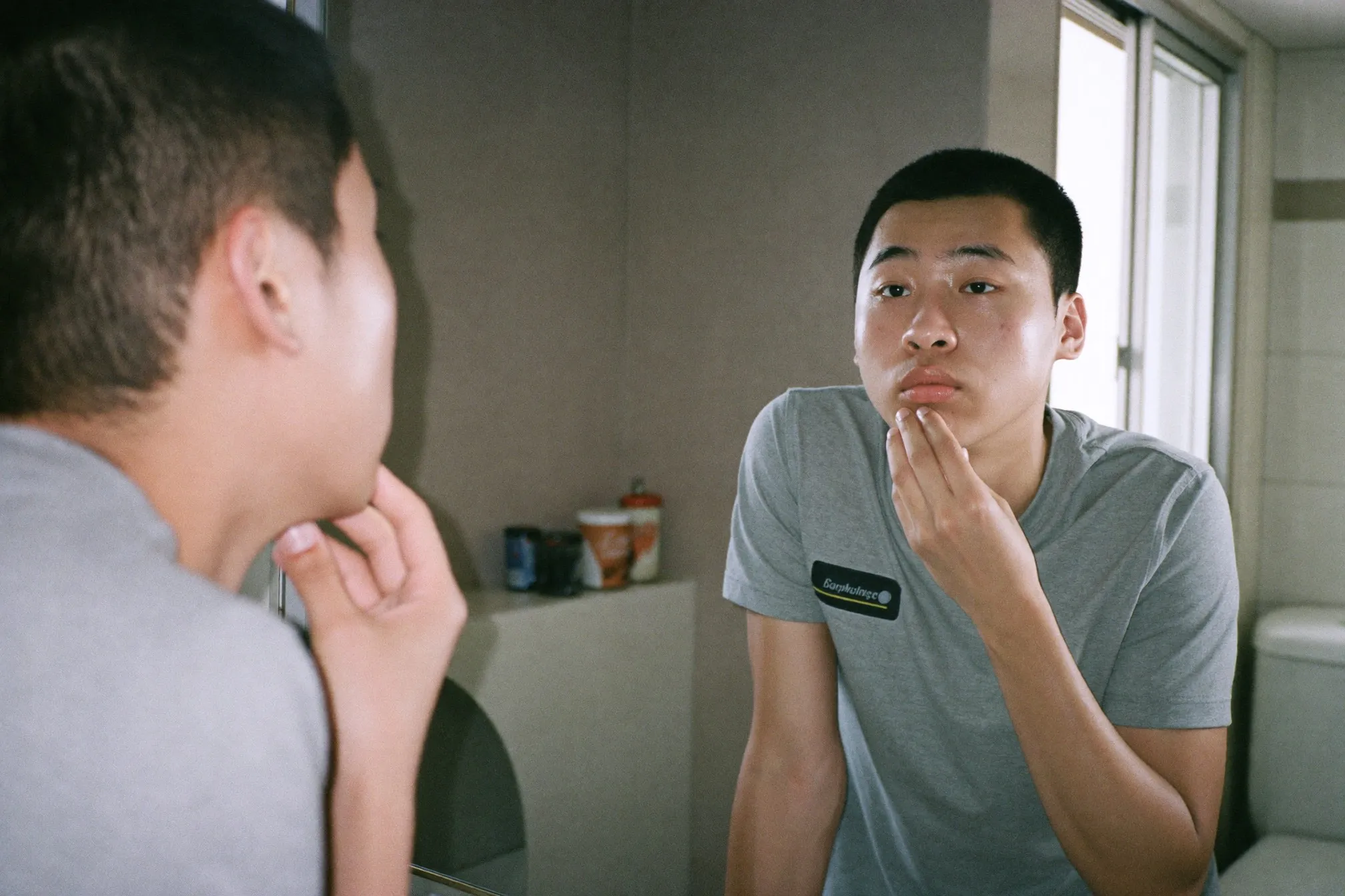 Young man checking his skin in the bathroom mirror of an HDB flat in the morning