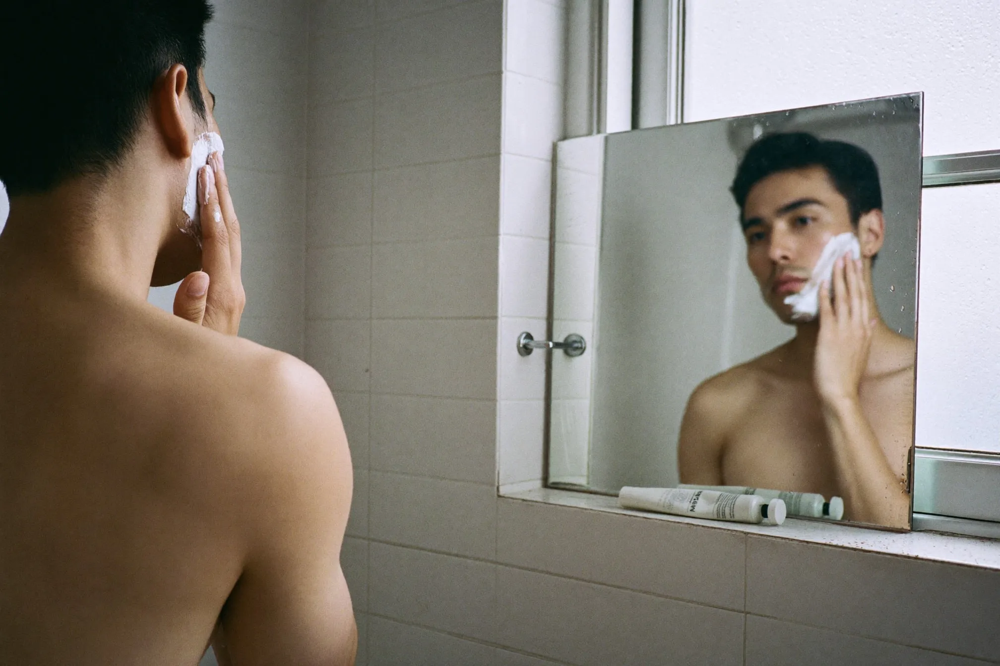 Man applying sunscreen with two fingers at a bathroom mirror in the morning
