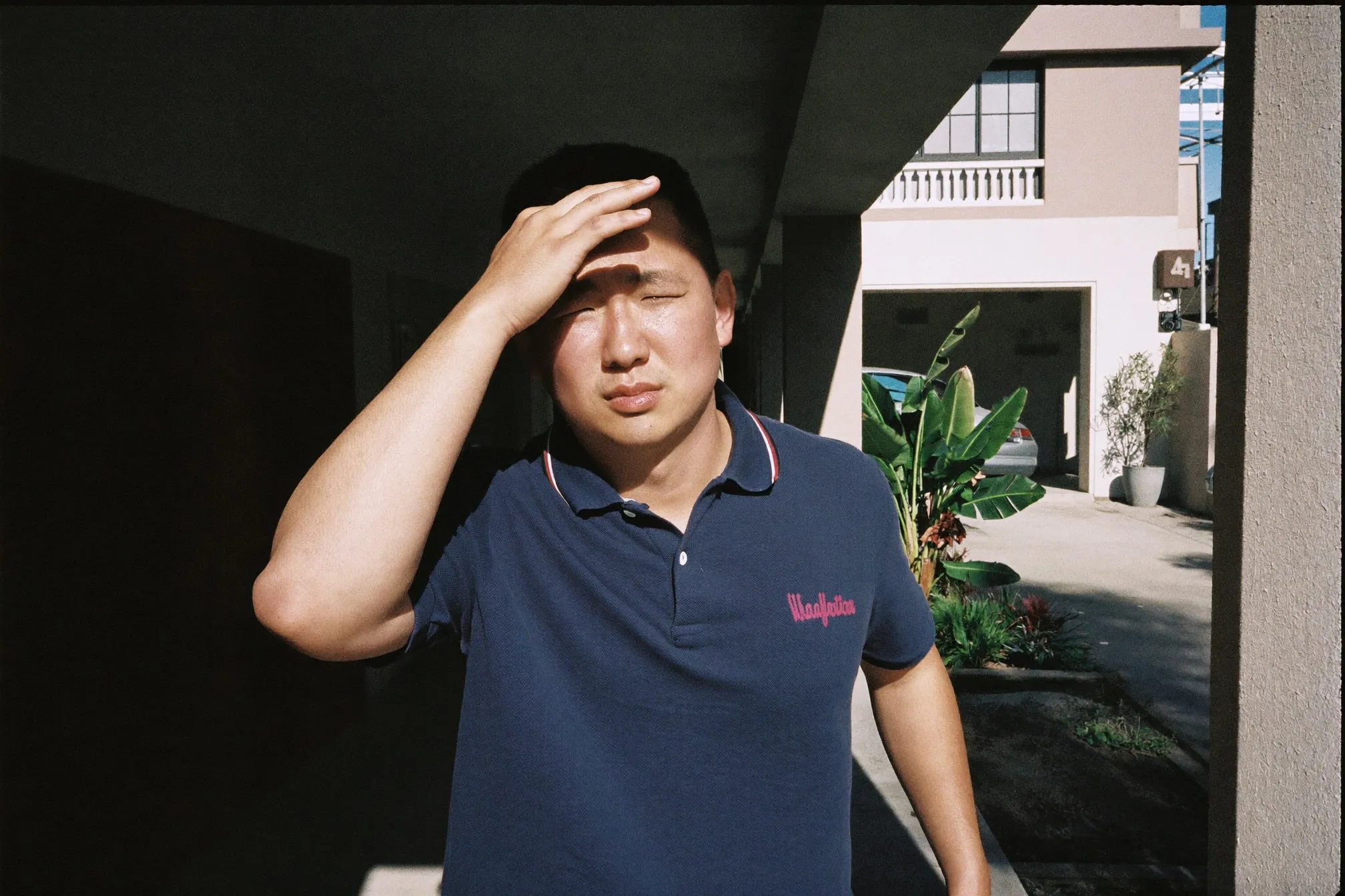 Man in his early thirties stepping out of an apartment block into bright morning sunlight