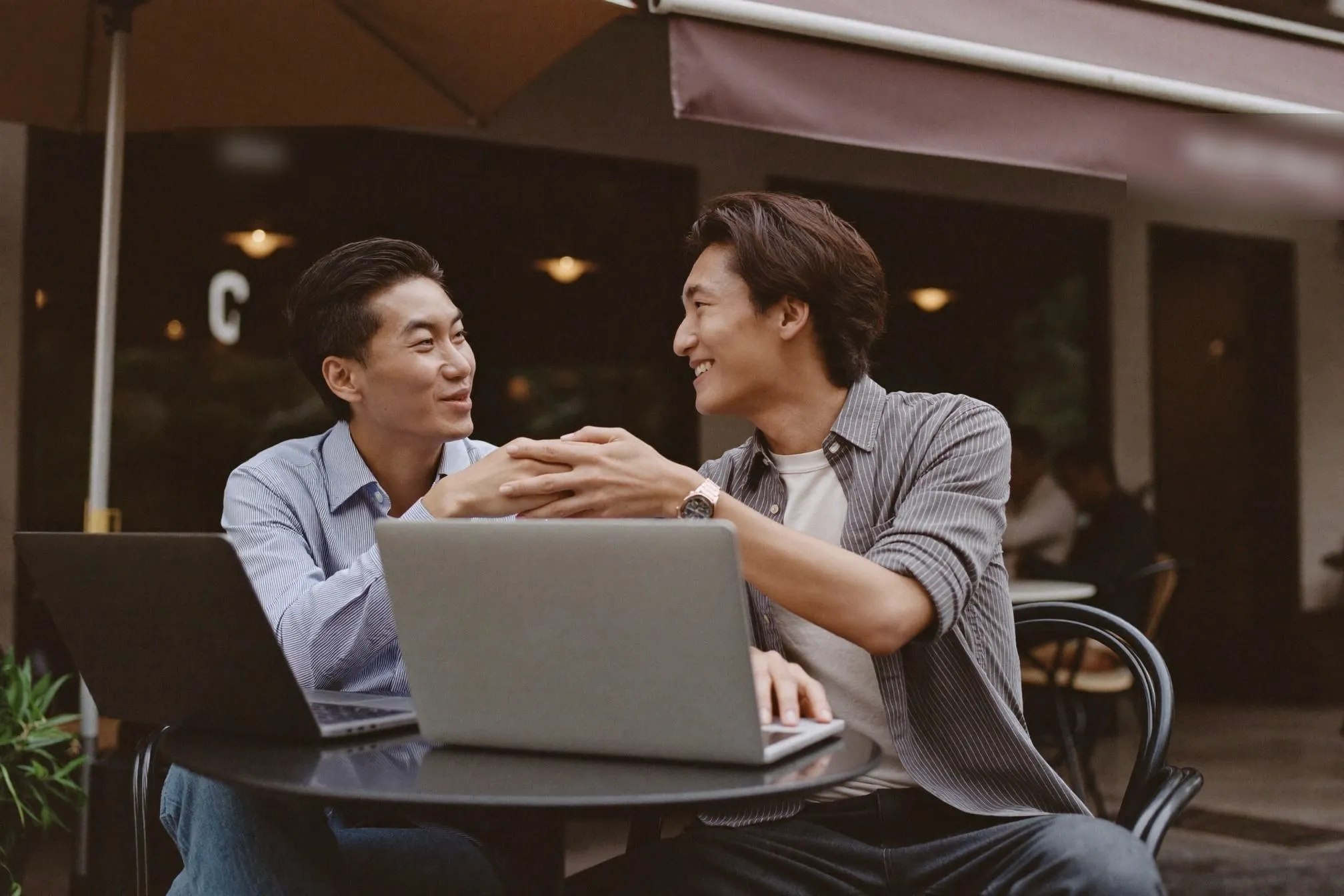 Two men in smart casual at an outdoor cafe meeting under a shophouse awning in Kuala Lumpur