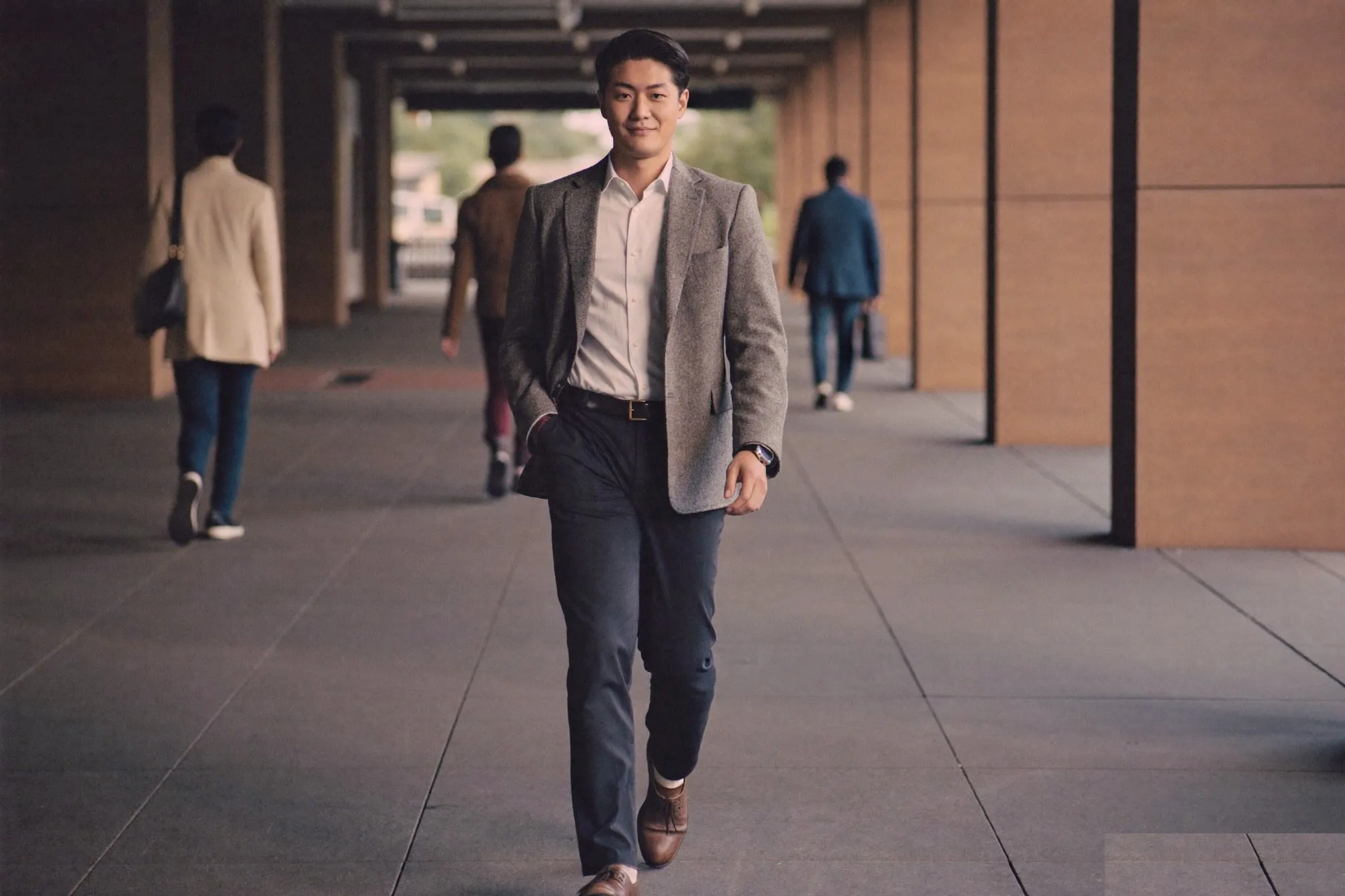 Man in an unstructured grey blazer, white oxford shirt and dark chinos walking through a covered walkway in Singapore's CBD