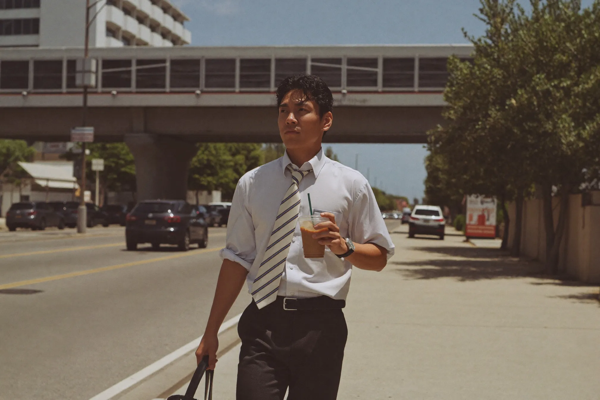 Man in office wear walking under midday tropical sun with an iced coffee