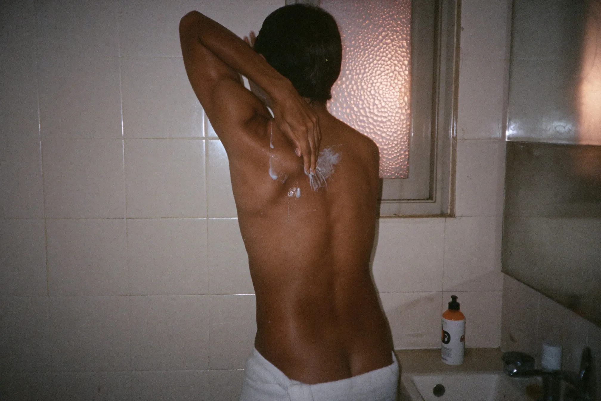 Man reaching over his shoulder to apply lotion to his upper back in a bathroom