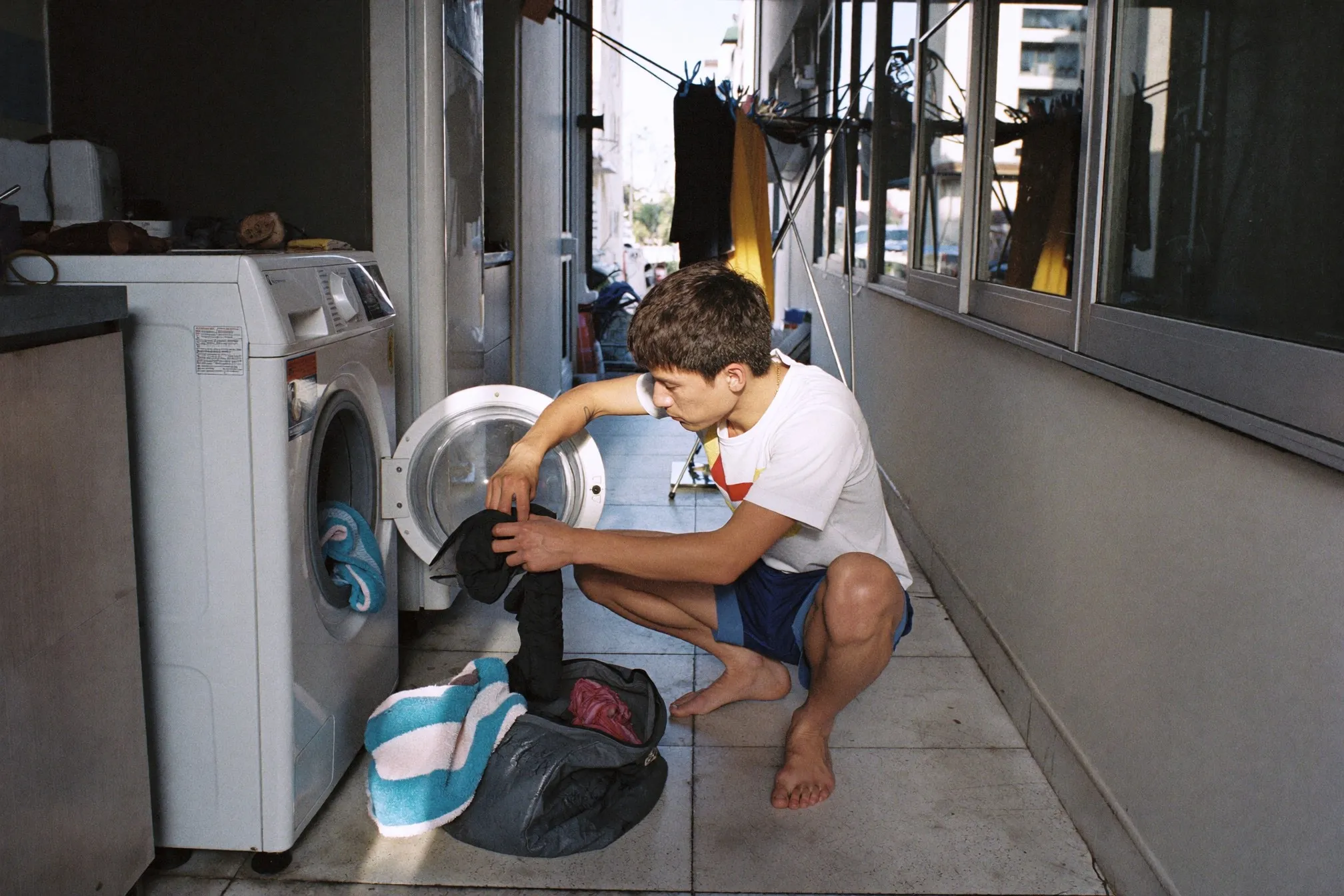 Man loading damp training clothes into a washing machine in an HDB service yard