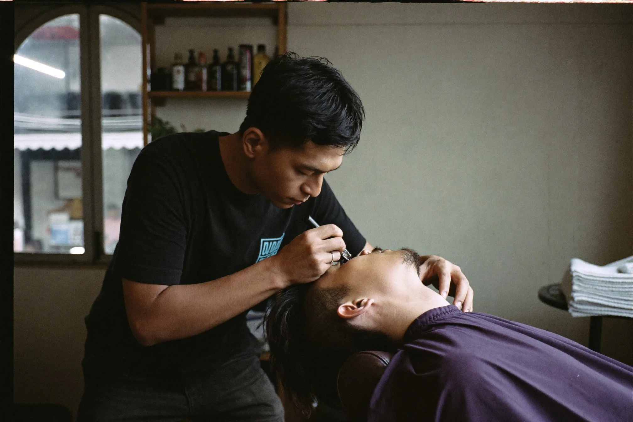 Barber shaping a client's beard neckline with a trimmer in a small barbershop