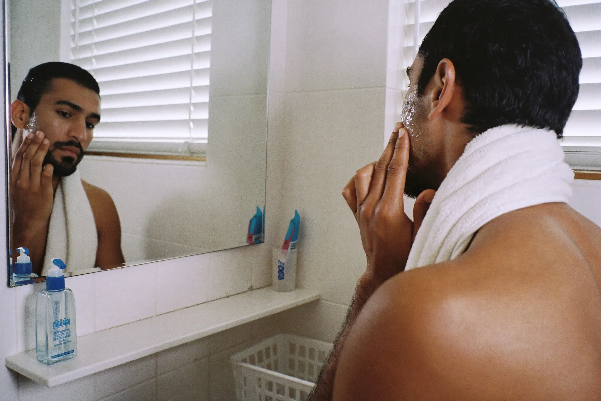Man applying a watery sunscreen gel to his face in an apartment bathroom before work