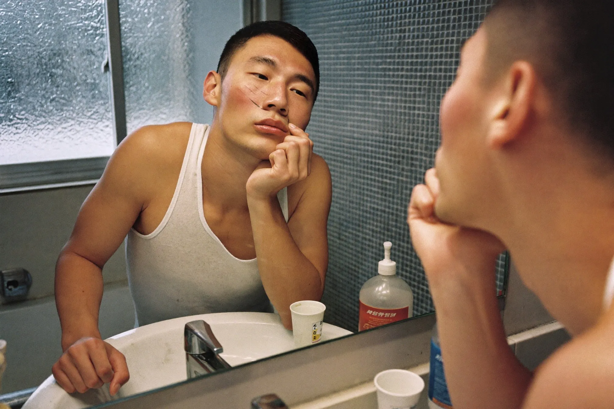 Man leaning close to a bathroom mirror inspecting the skin on his nose under morning light
