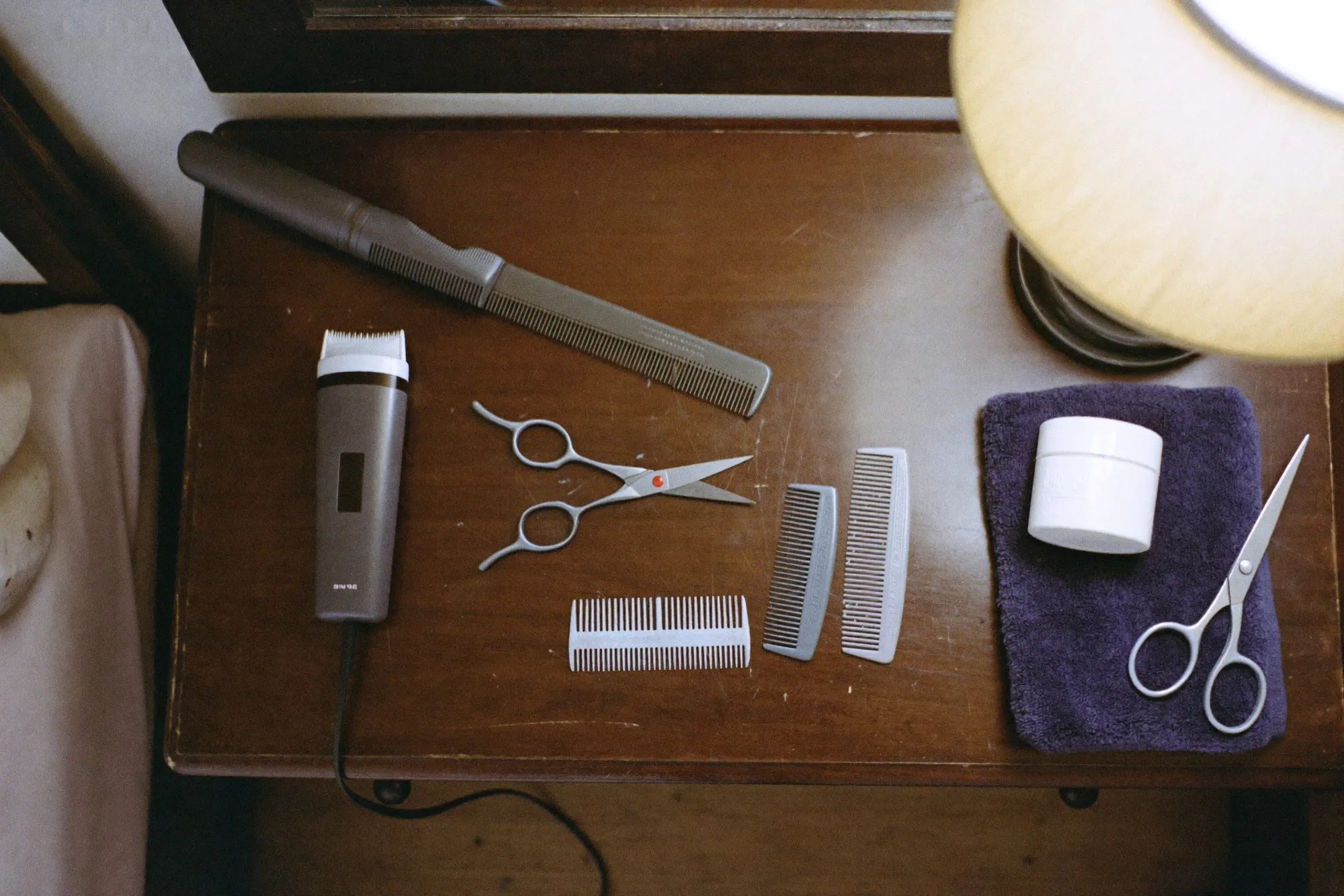 Flat lay of a cordless body trimmer, guard combs, a long-handled back trimmer and grooming scissors on a wooden dresser