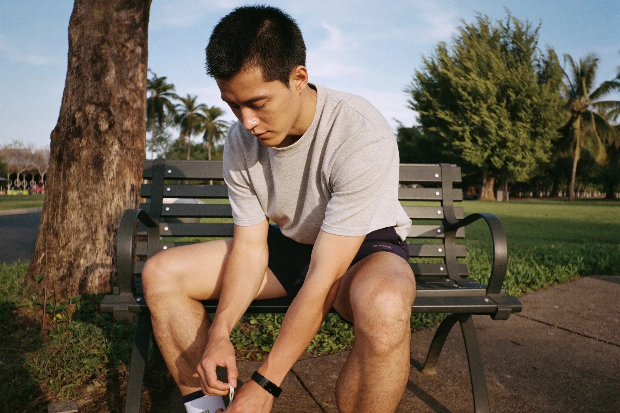 Man in running shorts and a t-shirt lacing his shoes on a bench at a Singapore park connector