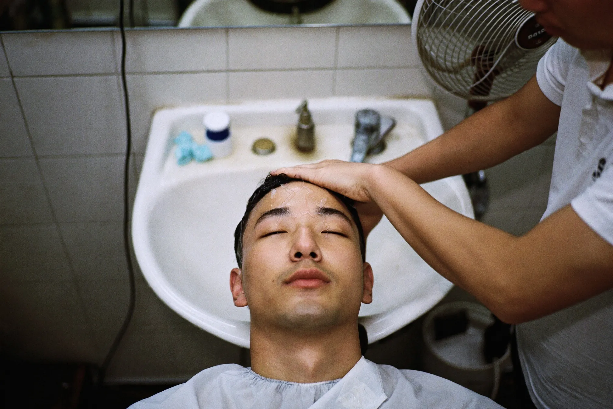 Man having his hair and scalp washed at a basin in a neighbourhood barbershop