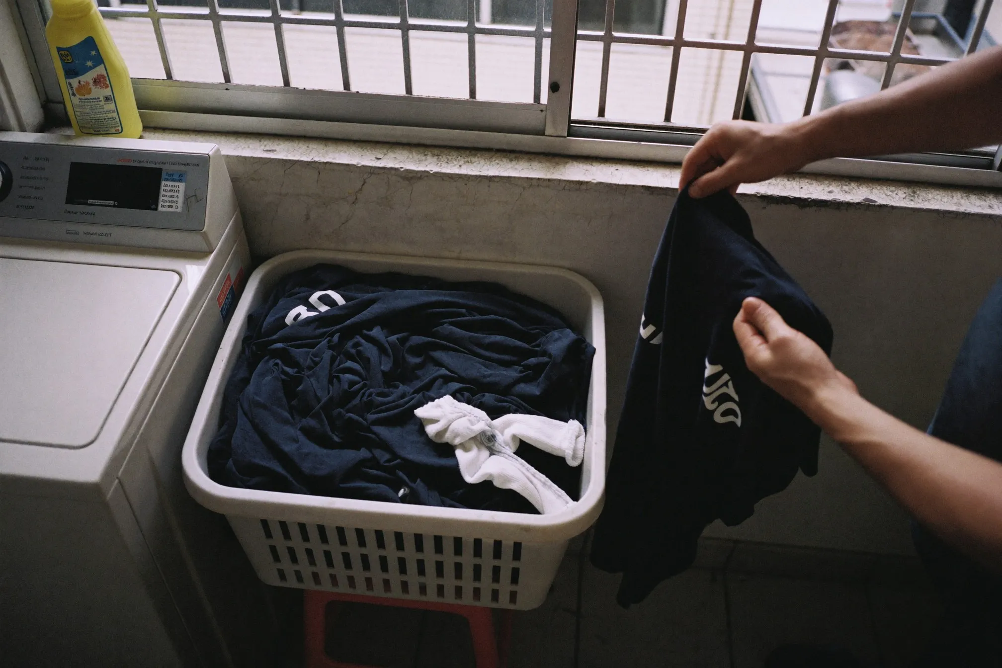 Laundry basket of worn gym shirts beside a washing machine in an HDB service yard