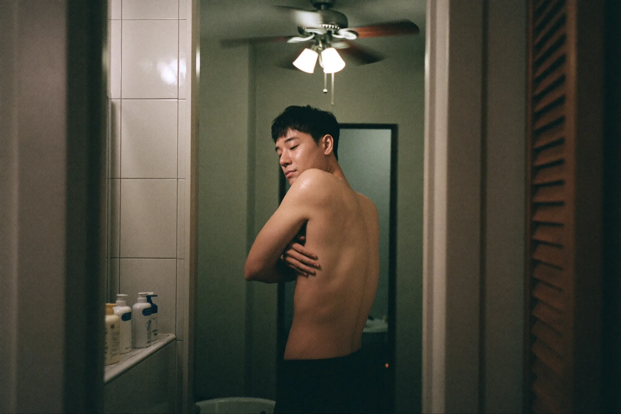 Man drying his shoulders with a towel in a small bathroom under a ceiling fan after showering