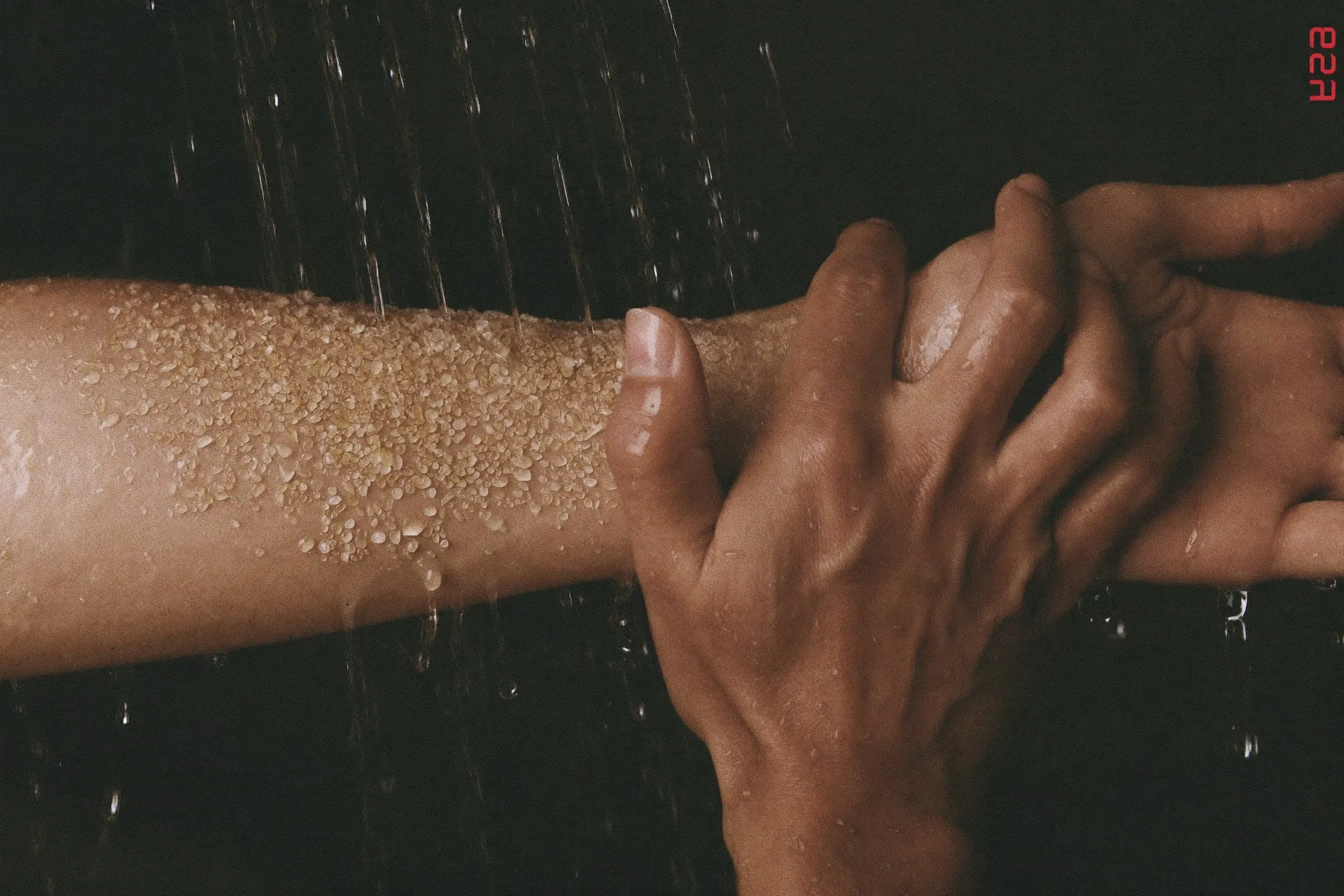 Close view of scrub granules spread across a damp forearm under shower water