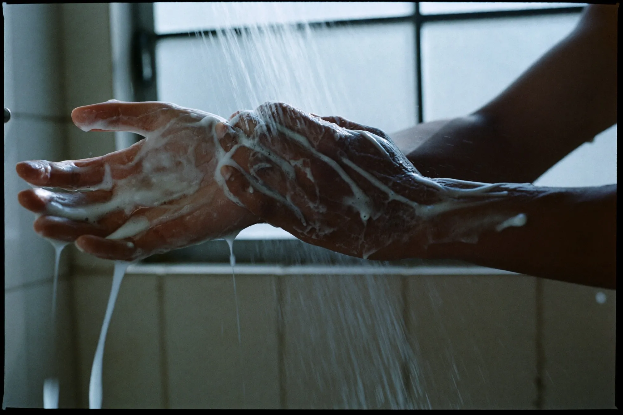 Close view of body wash lathered on a man's forearm under running water