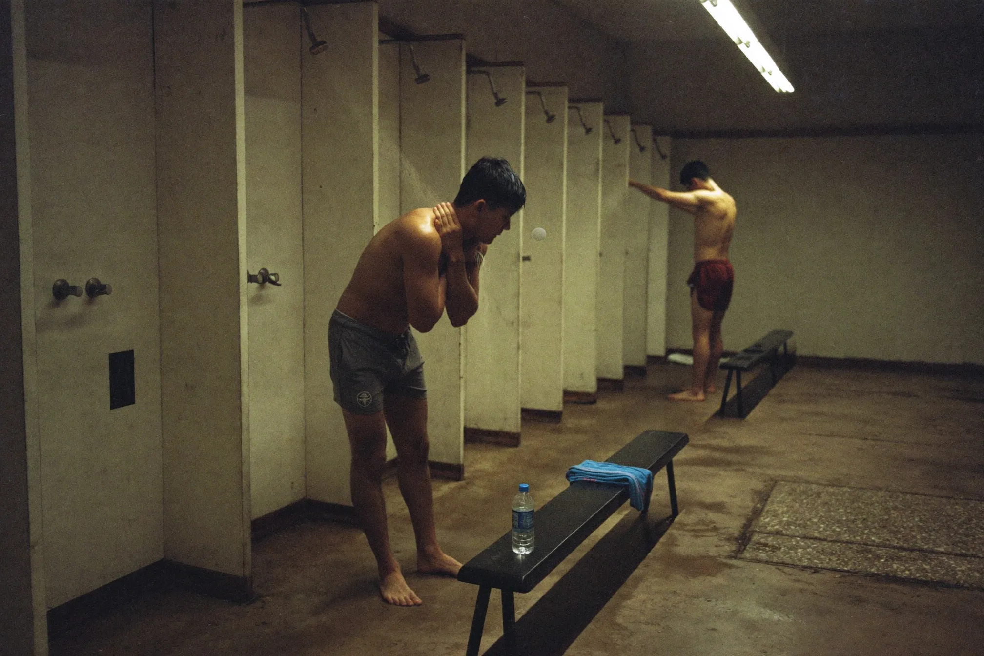 Men rinsing off in a gym changing room shower area after a futsal session