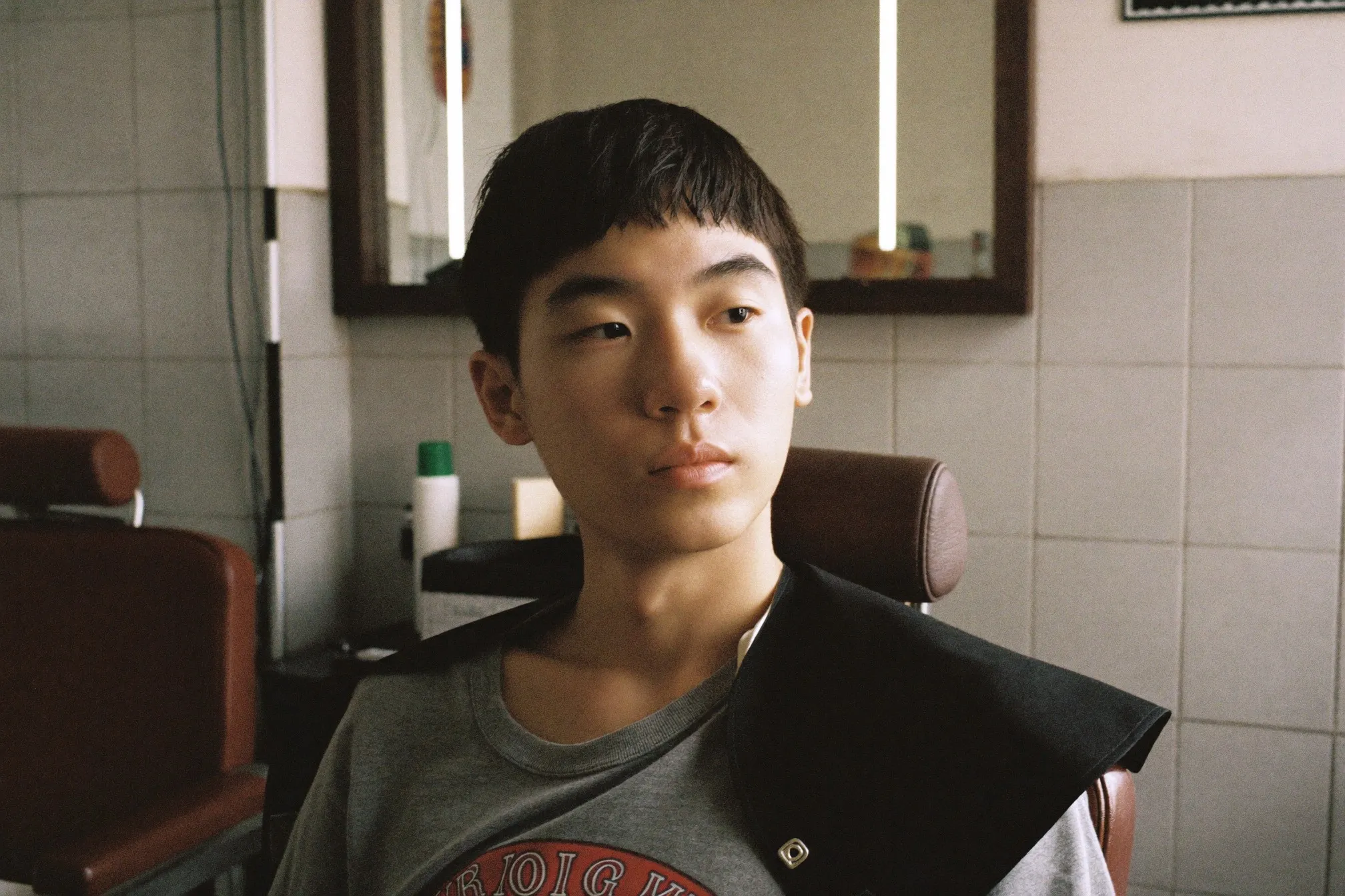 Young Chinese Malaysian man with a soft boyish haircut and light textured fringe sitting in a KL barbershop chair after his cut