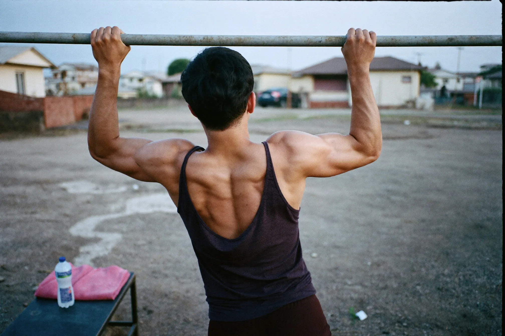 Malay man in his late twenties doing pull-ups on a bar at an outdoor fitness corner in a Singapore HDB estate at dawn