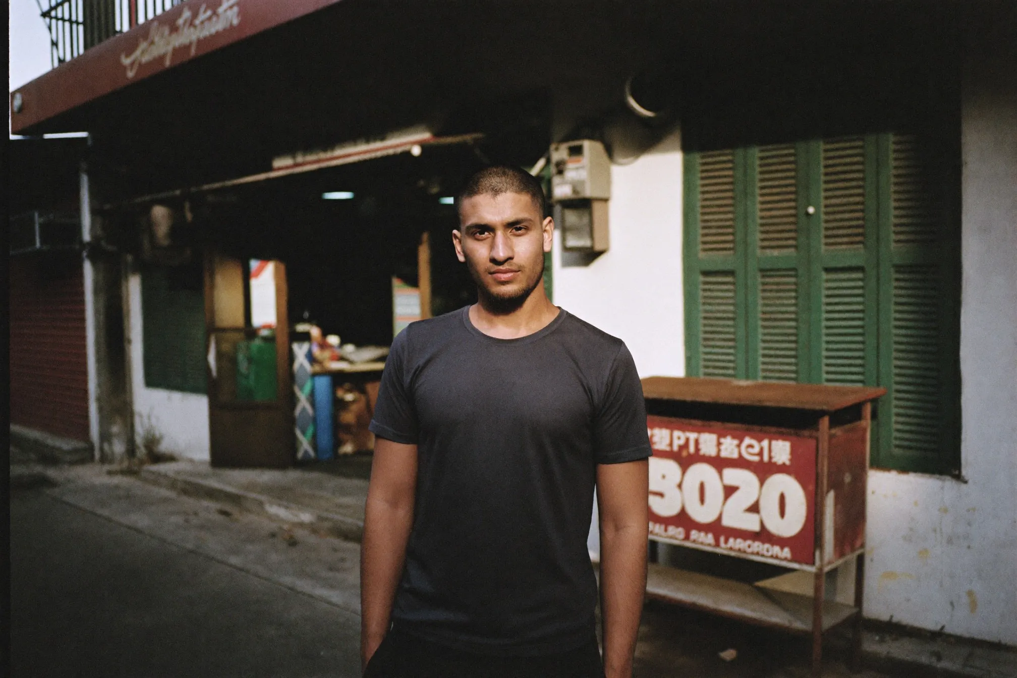 Man with a fresh grade two buzz cut standing outside a shophouse barbershop in Kuala Lumpur
