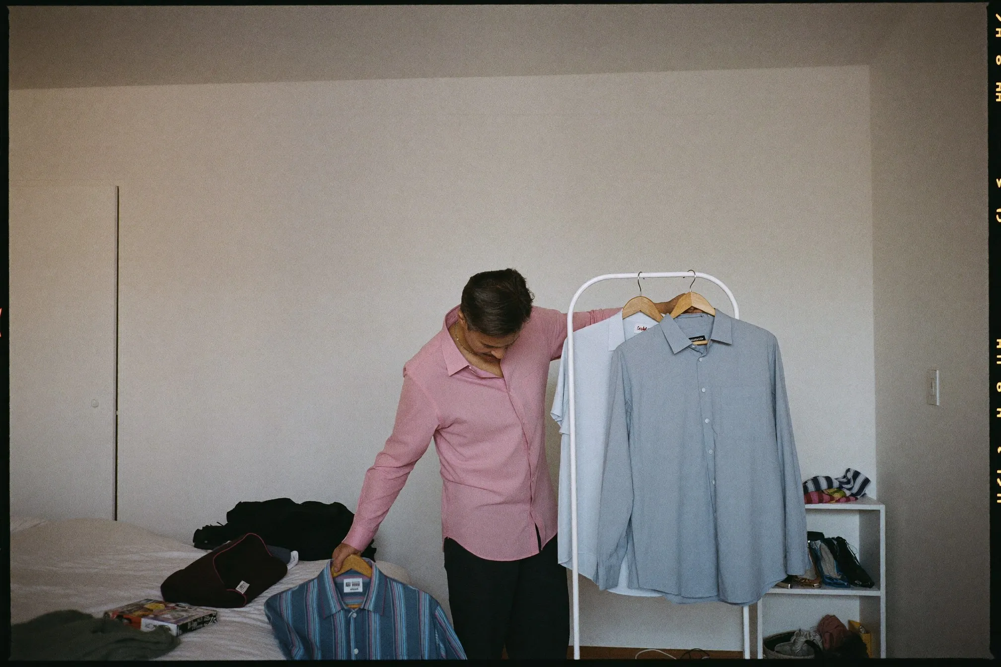 Man choosing between two shirts from a small tidy clothes rail in a bright bedroom