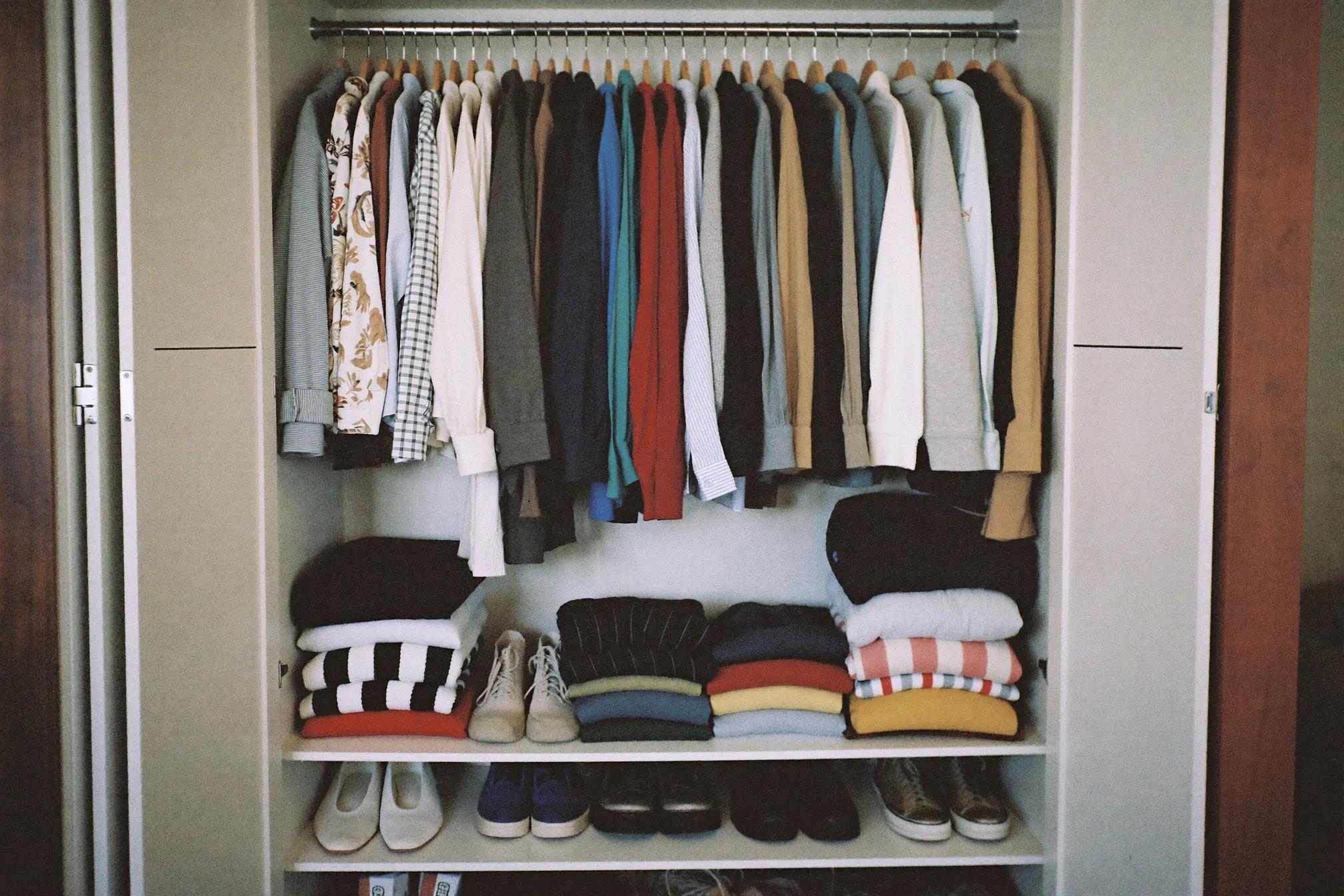 Neatly organised open wardrobe with a short rail of shirts, folded tees and two pairs of shoes below