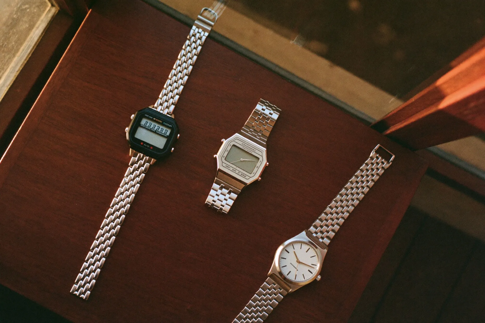 Three generic digital and ana-digi watches in resin and steel laid out on a wooden table in window light
