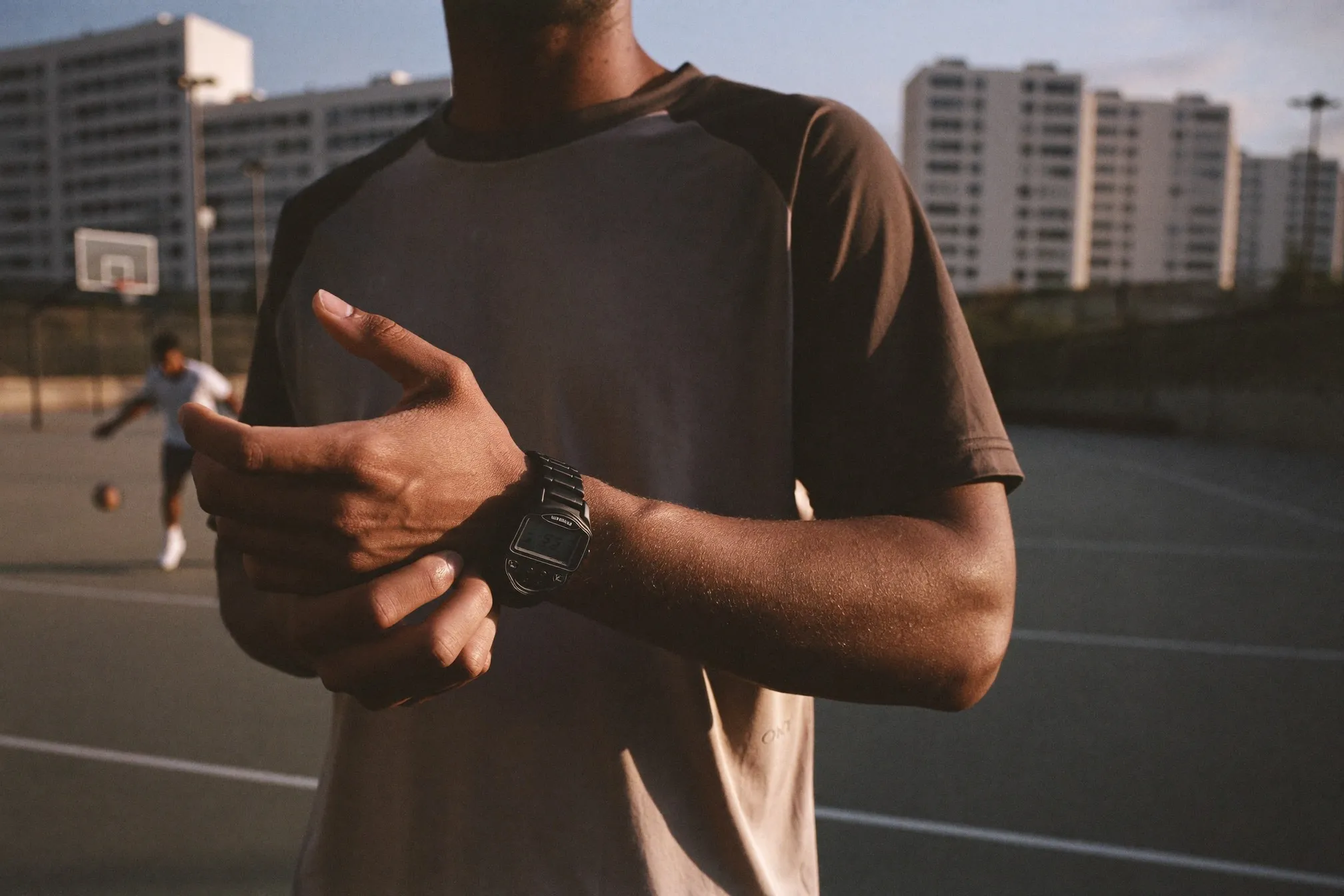 Man checking a rugged resin digital watch courtside at an outdoor basketball court in Singapore