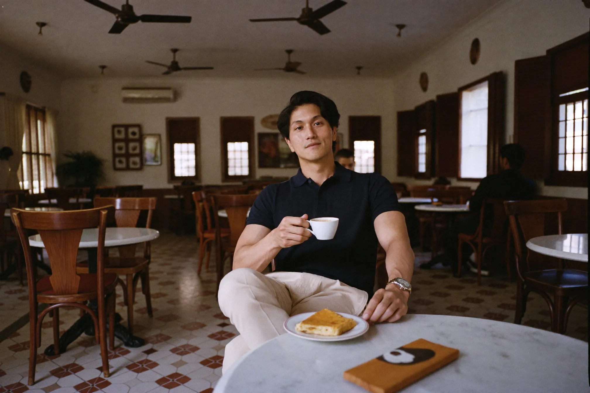 Man in a plain navy polo and beige chinos having kopi and kaya toast at a marble-top kopitiam table