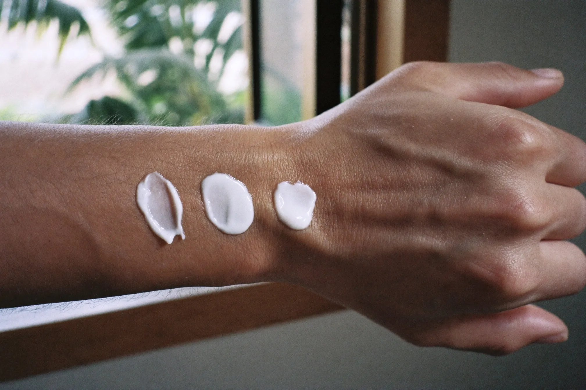 Three thick blobs of white moisturiser cream on the back of a man's hand, one already rubbed in