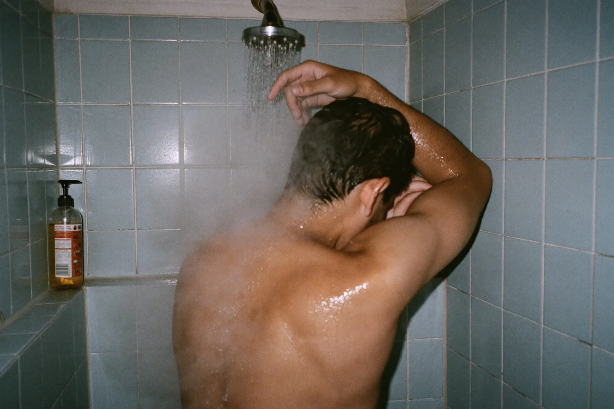 Man rinsing his shoulders and upper back under a shower in a small HDB bathroom