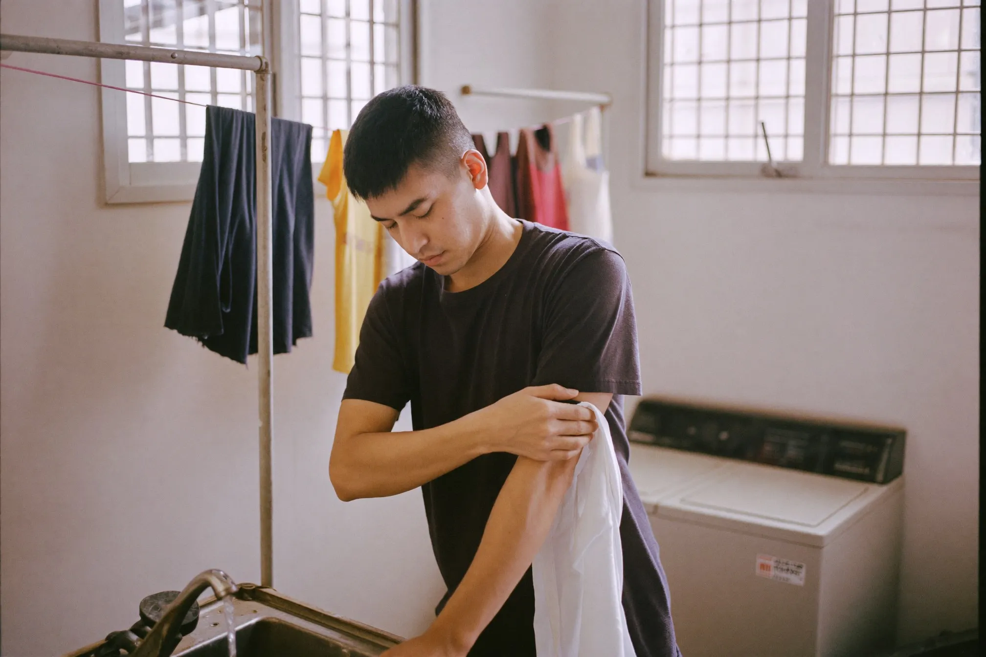 Man treating the underarm of a white shirt at a laundry sink in an HDB service yard