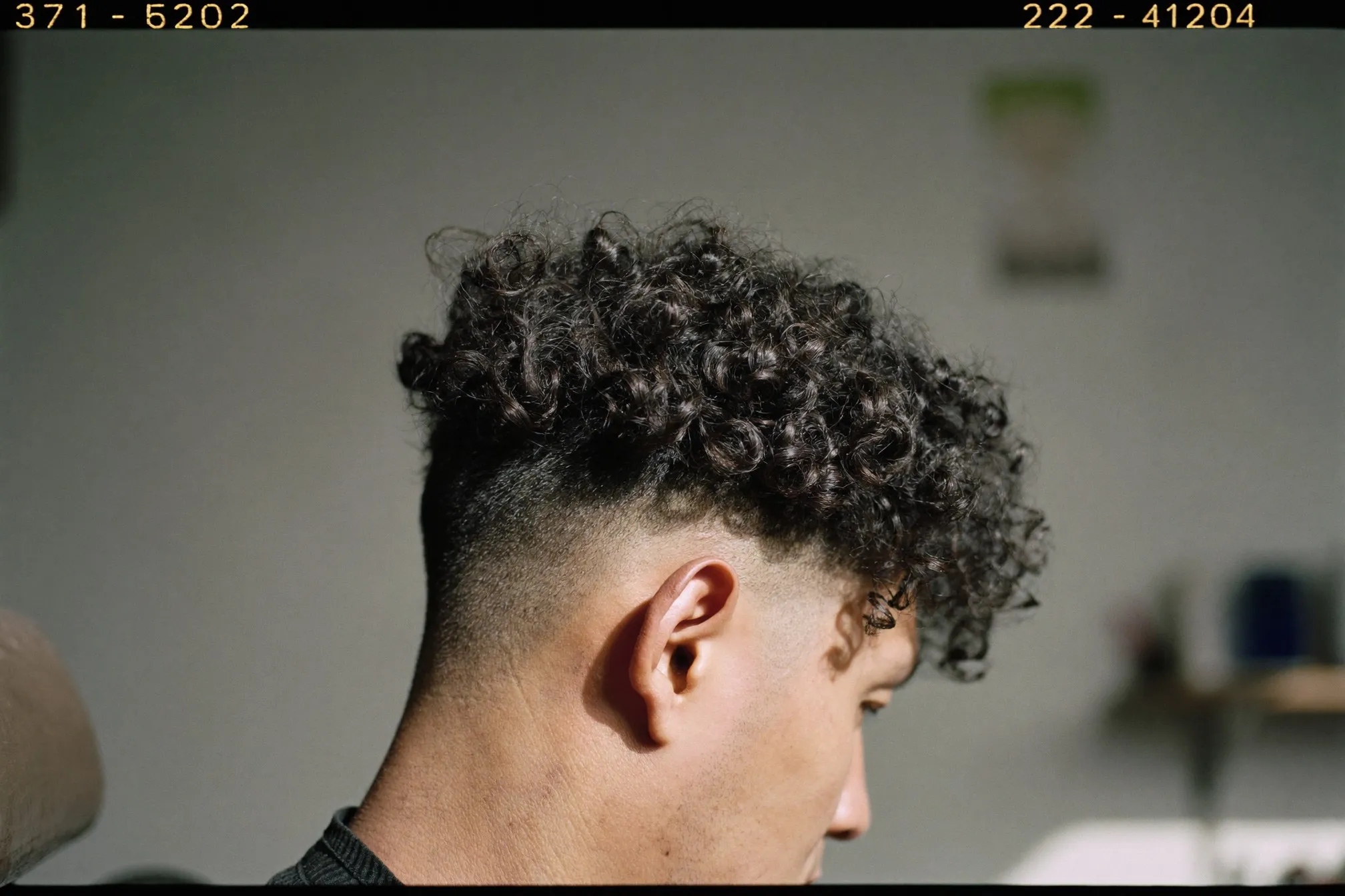 Close side view of a Chinese Malaysian man's defined dark curls with a tapered barber cut at the sides