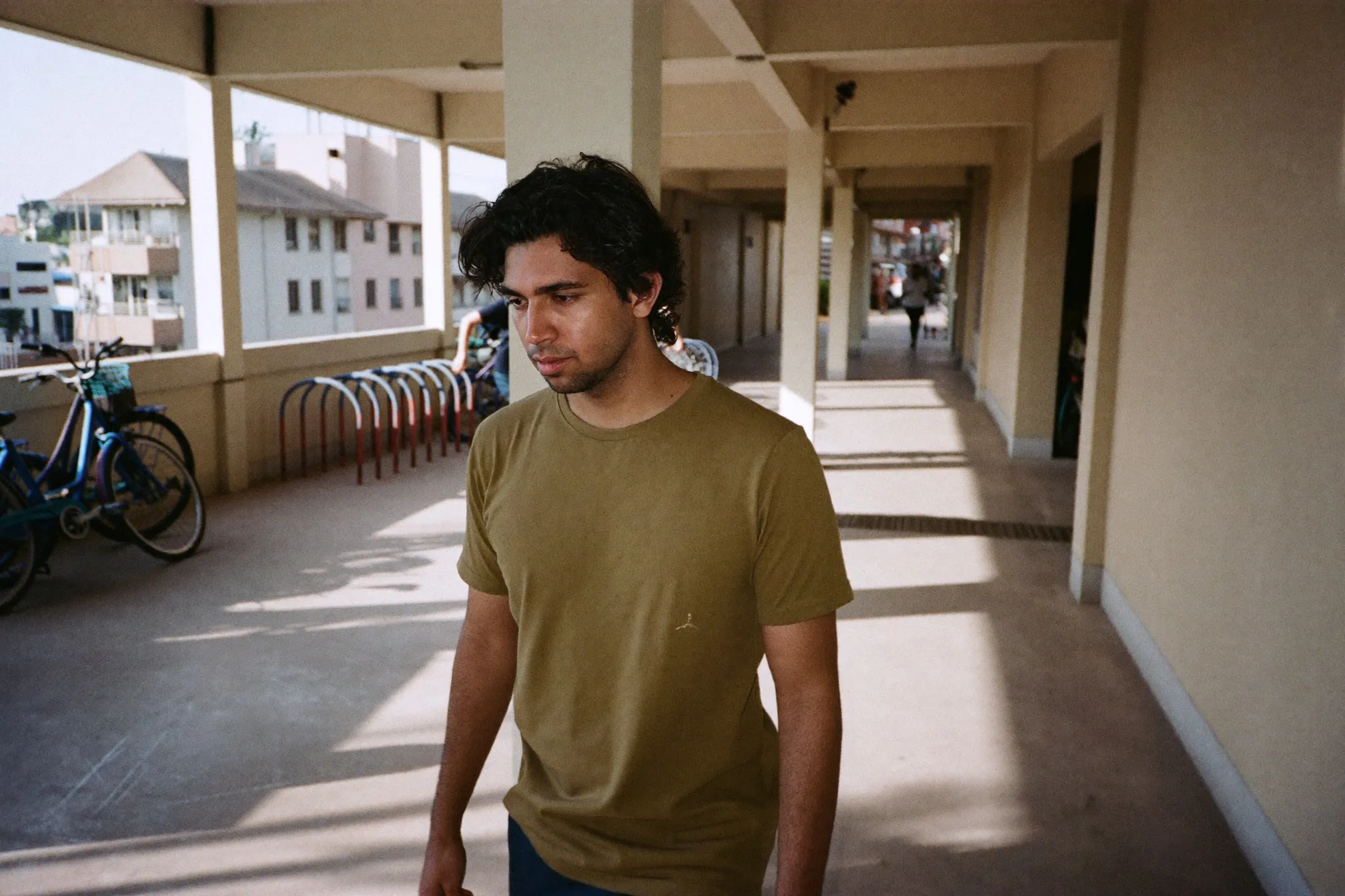 Indian Singaporean man with wavy hair walking through an HDB void deck in the afternoon