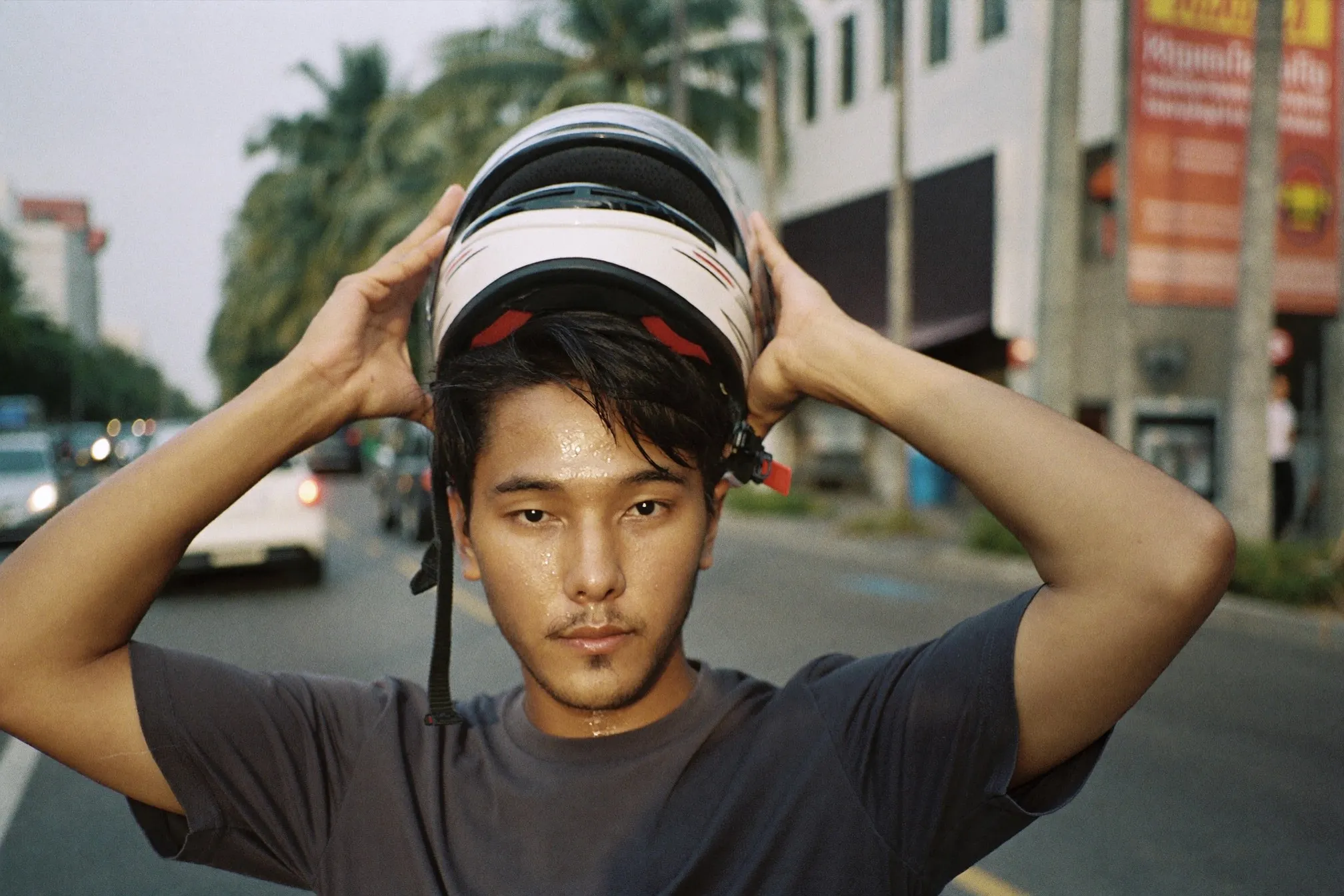 Motorcyclist lifting off his helmet at a roadside stop in Kuala Lumpur, hair flattened and damp with sweat
