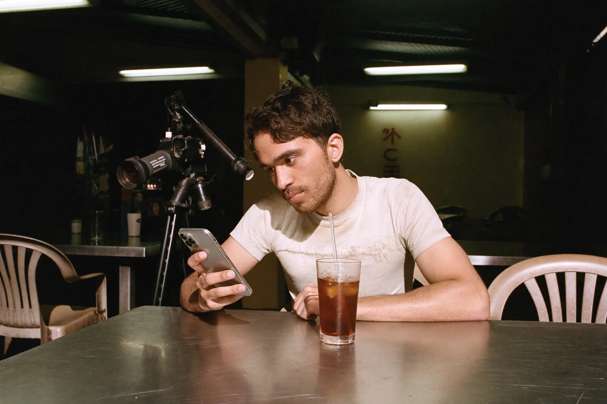 Man scrolling his phone over an iced drink at an open-air mamak late at night