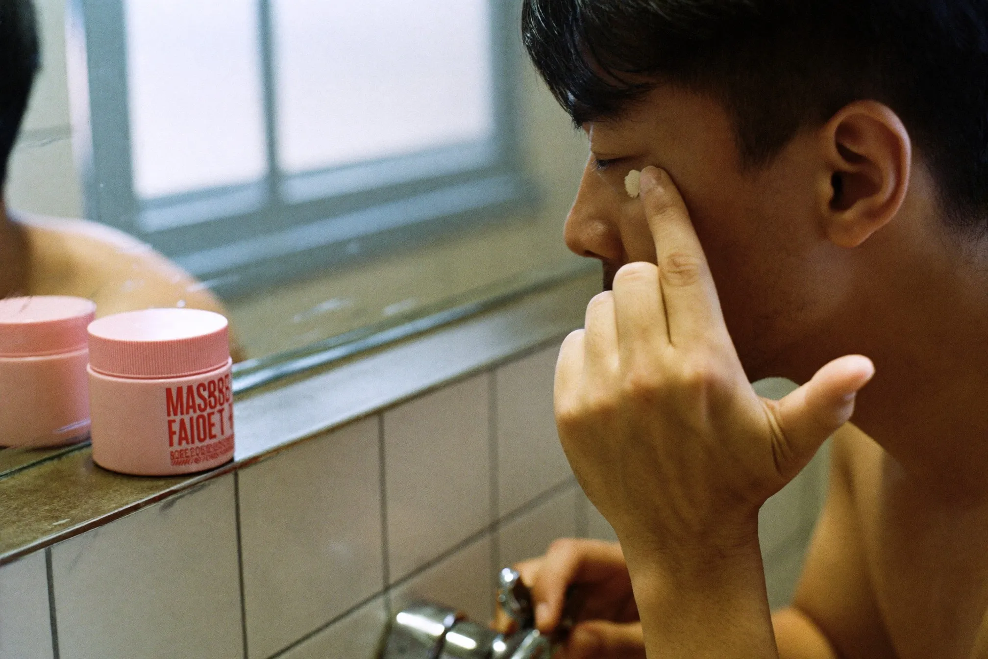 Close view of a man tapping a small amount of eye cream under his eye with his ring finger