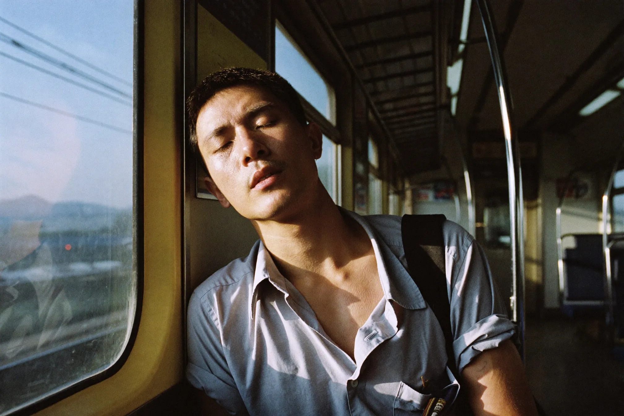 Man leaning against the door glass of a commuter train at dawn with visible shadows under his eyes