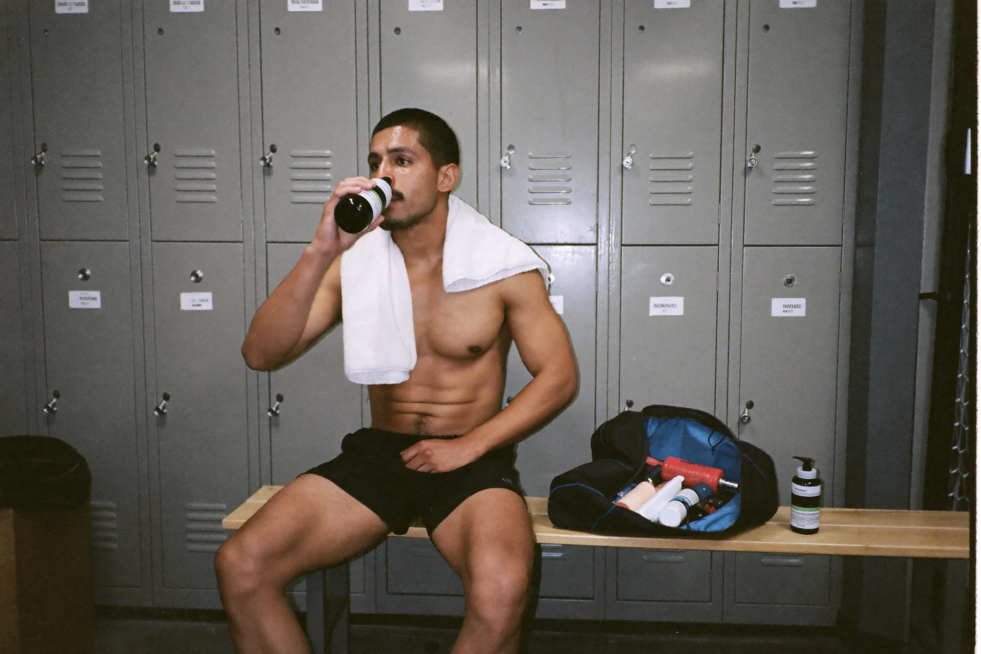Freshly showered man in a gym changing room with a towel over his shoulders and an open gym bag on the bench
