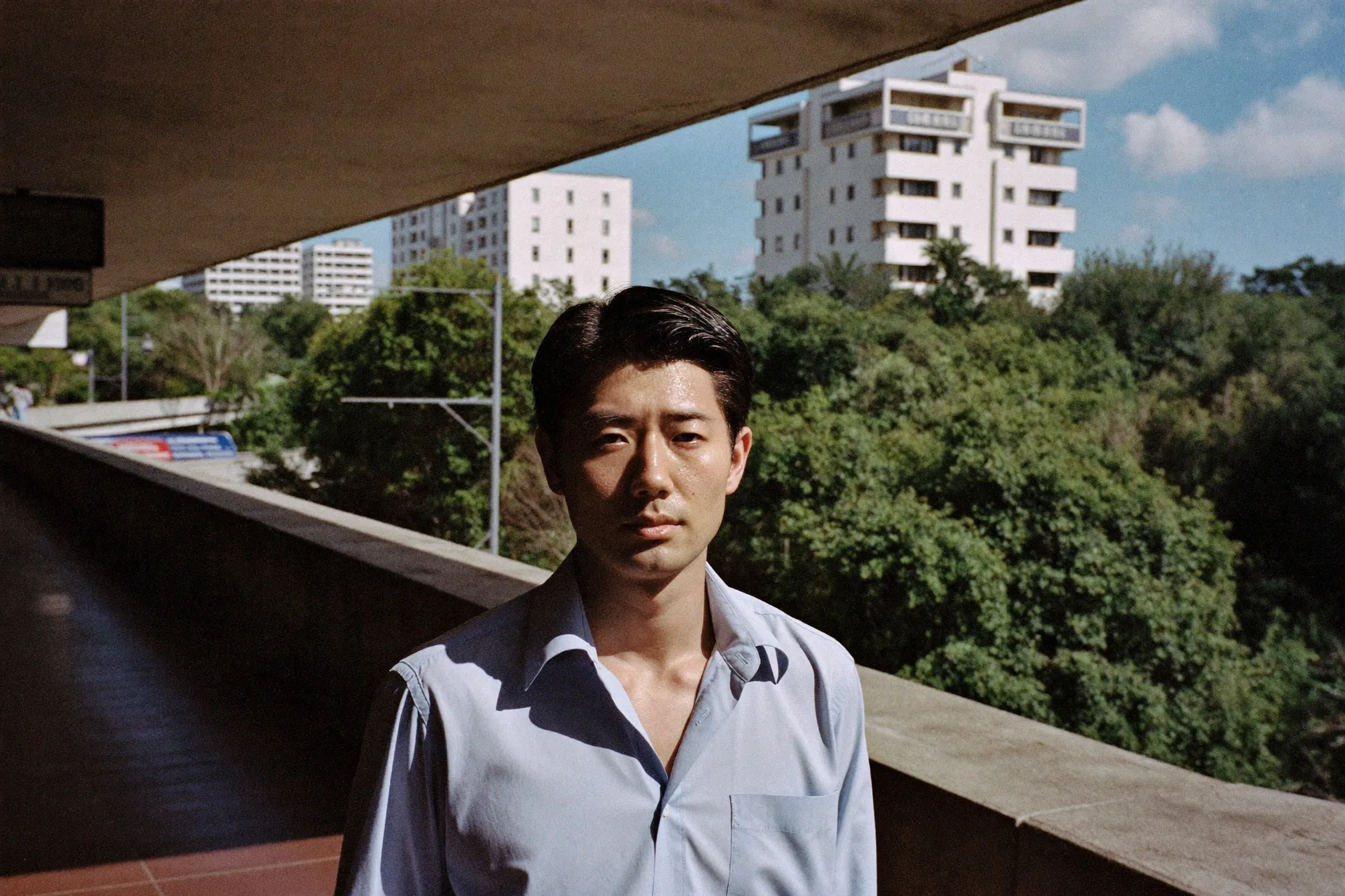Man in a light office shirt walking along a covered walkway near an MRT station in harsh midday tropical heat