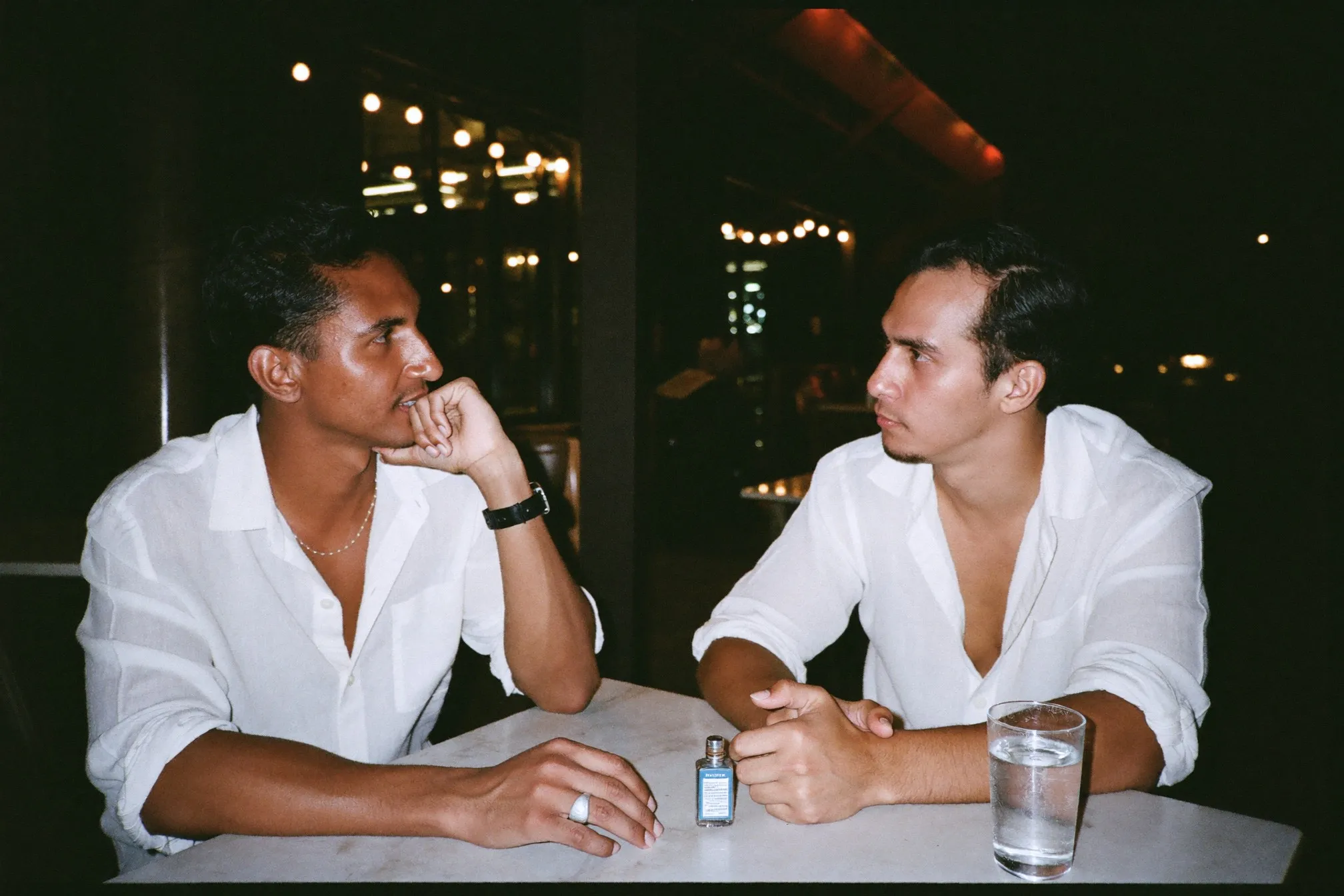 Two men talking at an outdoor shophouse cafe in the evening with a small travel atomiser on the table