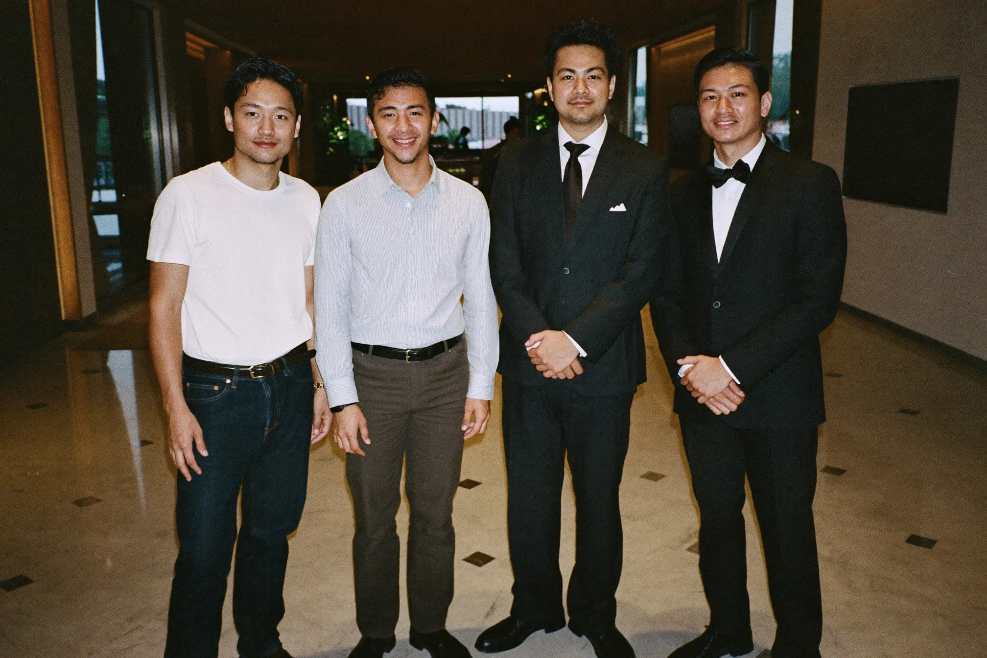 Four men in casual, smart casual, business formal and black tie standing together in a hotel lobby in Kuala Lumpur