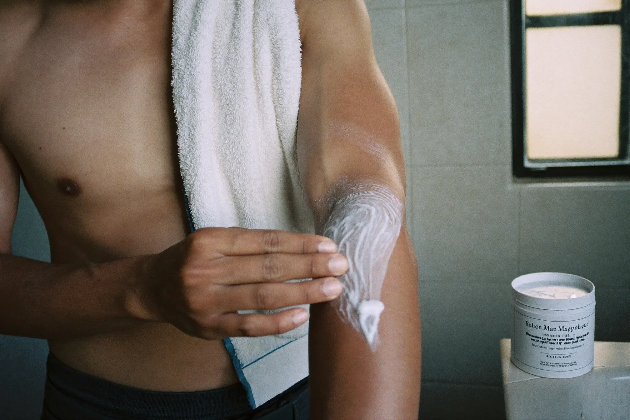 Close view of a man smoothing plain white moisturiser onto the inside of his elbow in a bathroom