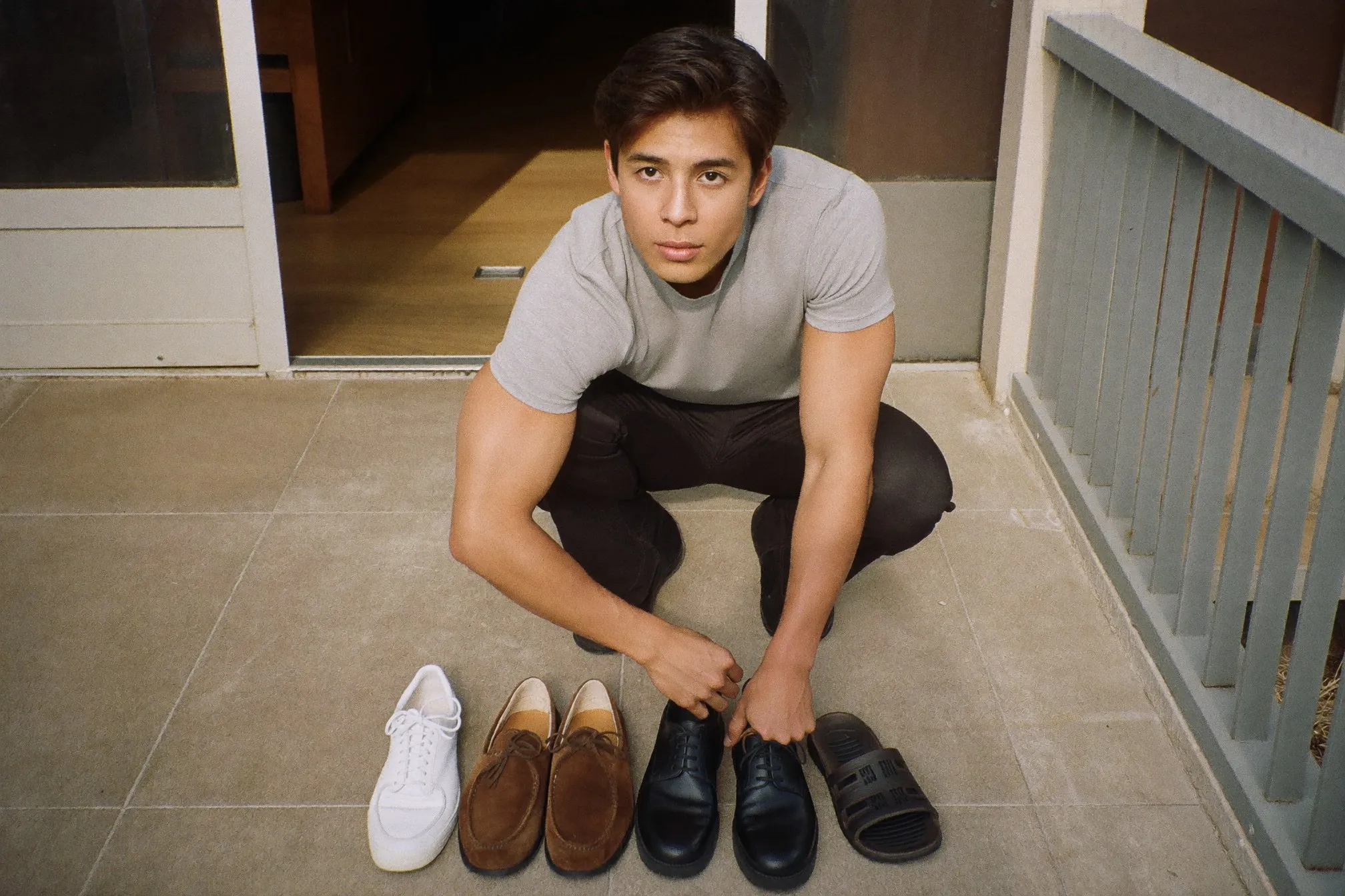 Man crouched at the doorway of an HDB flat with four pairs of shoes lined up on the corridor floor beside him