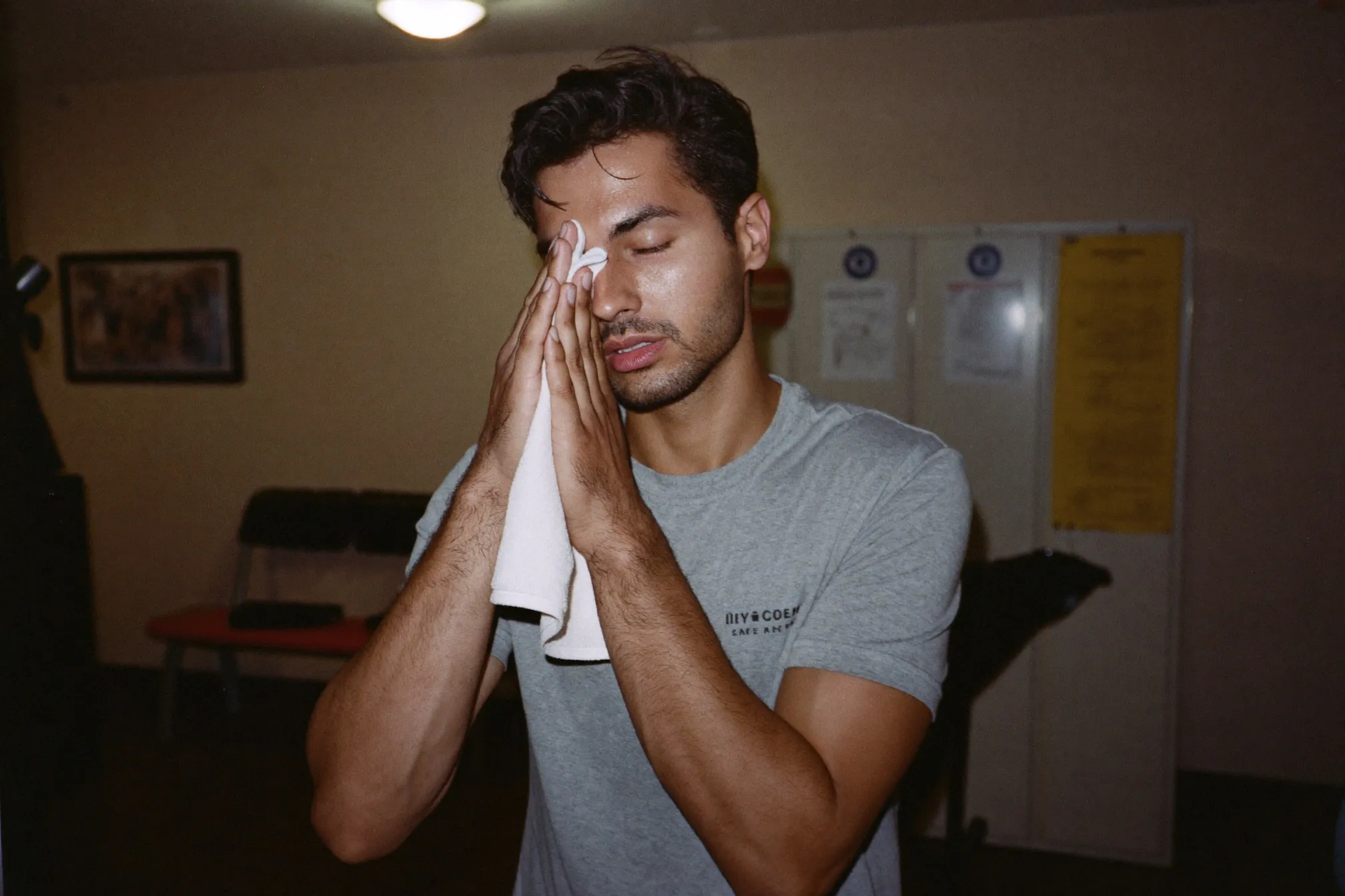 Man in sports wear wiping his face with a towel in a gym changing room