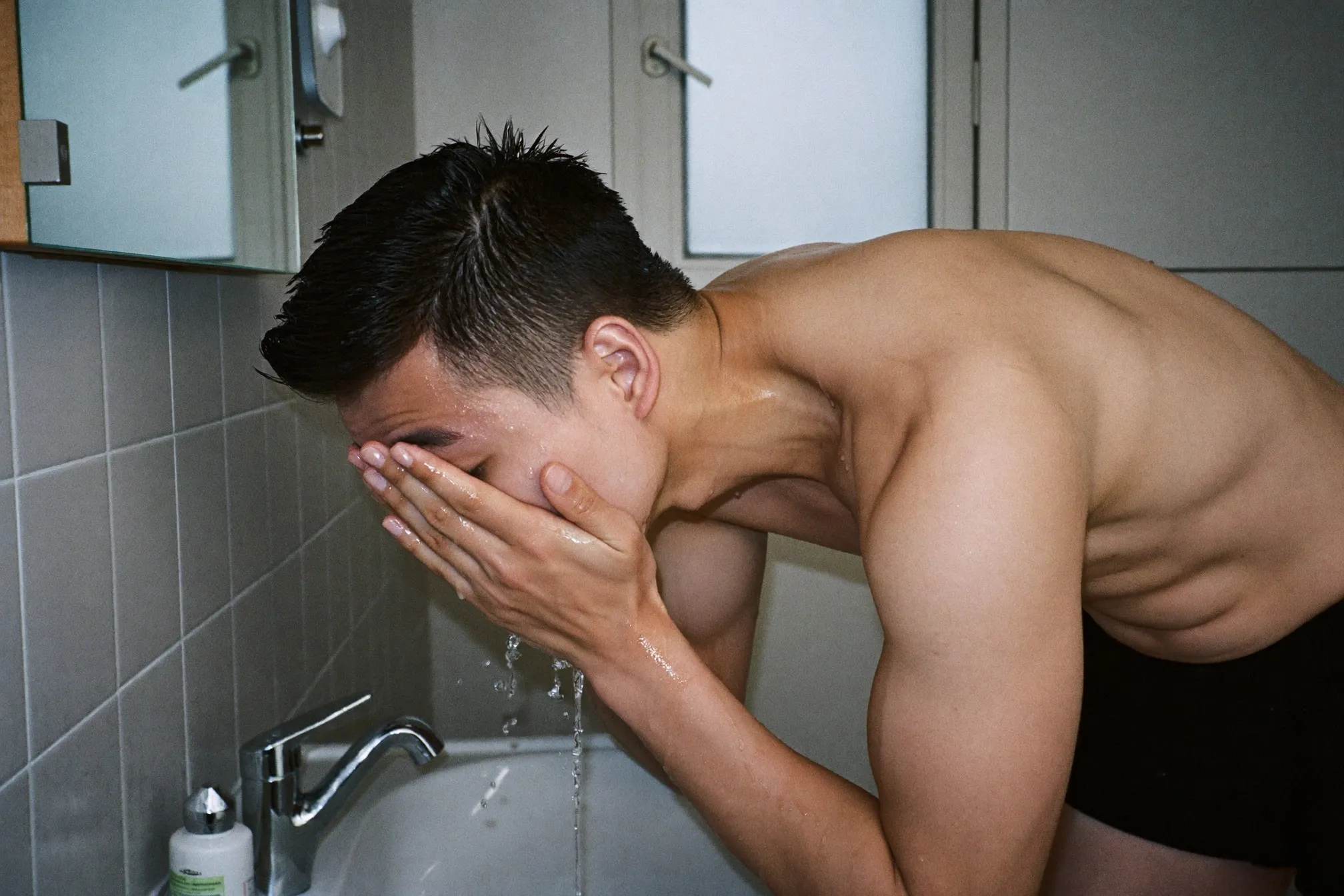 Man rinsing his face with water over a bathroom sink in the morning
