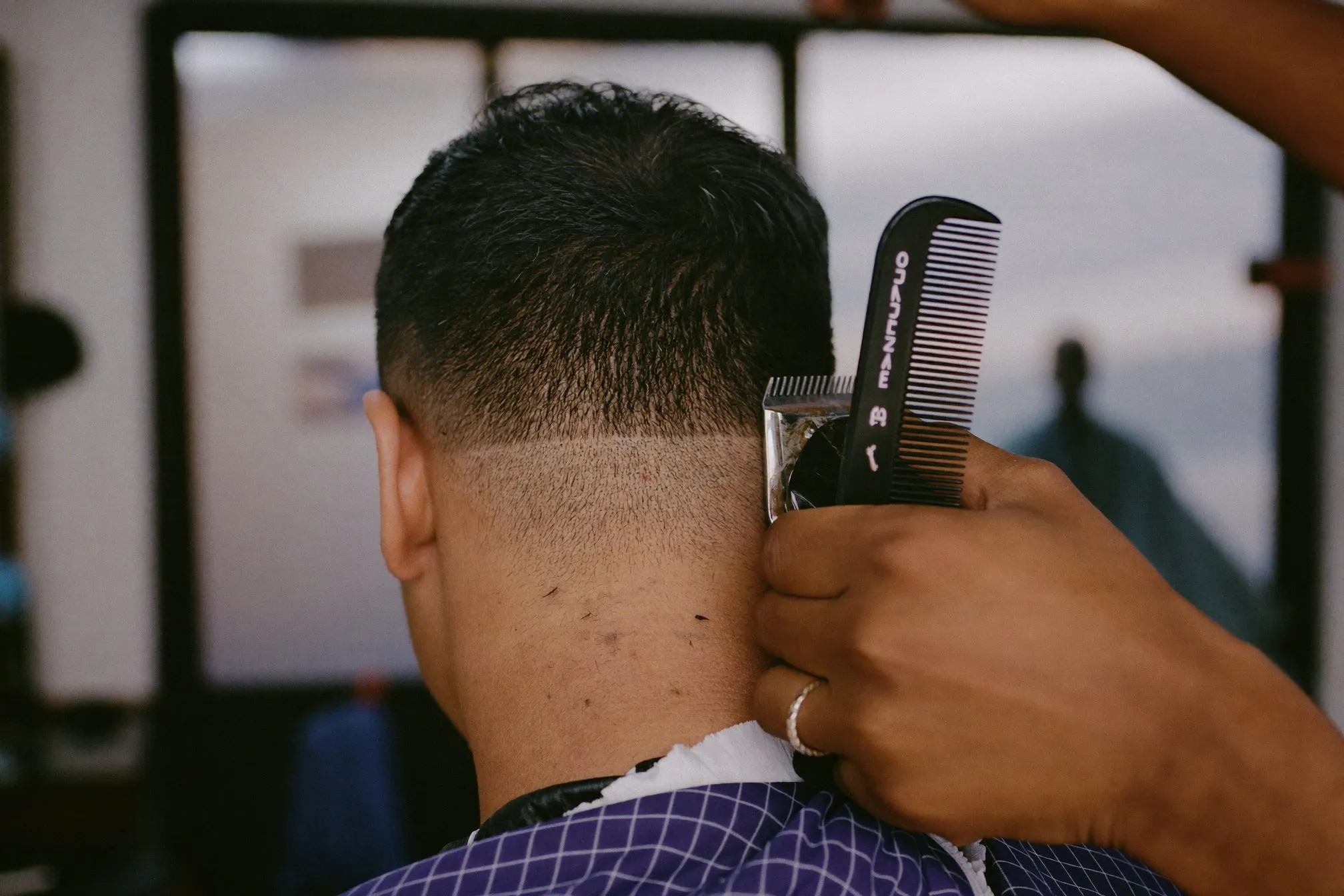 Close view of a barber blending a fade above the ear with clipper and comb